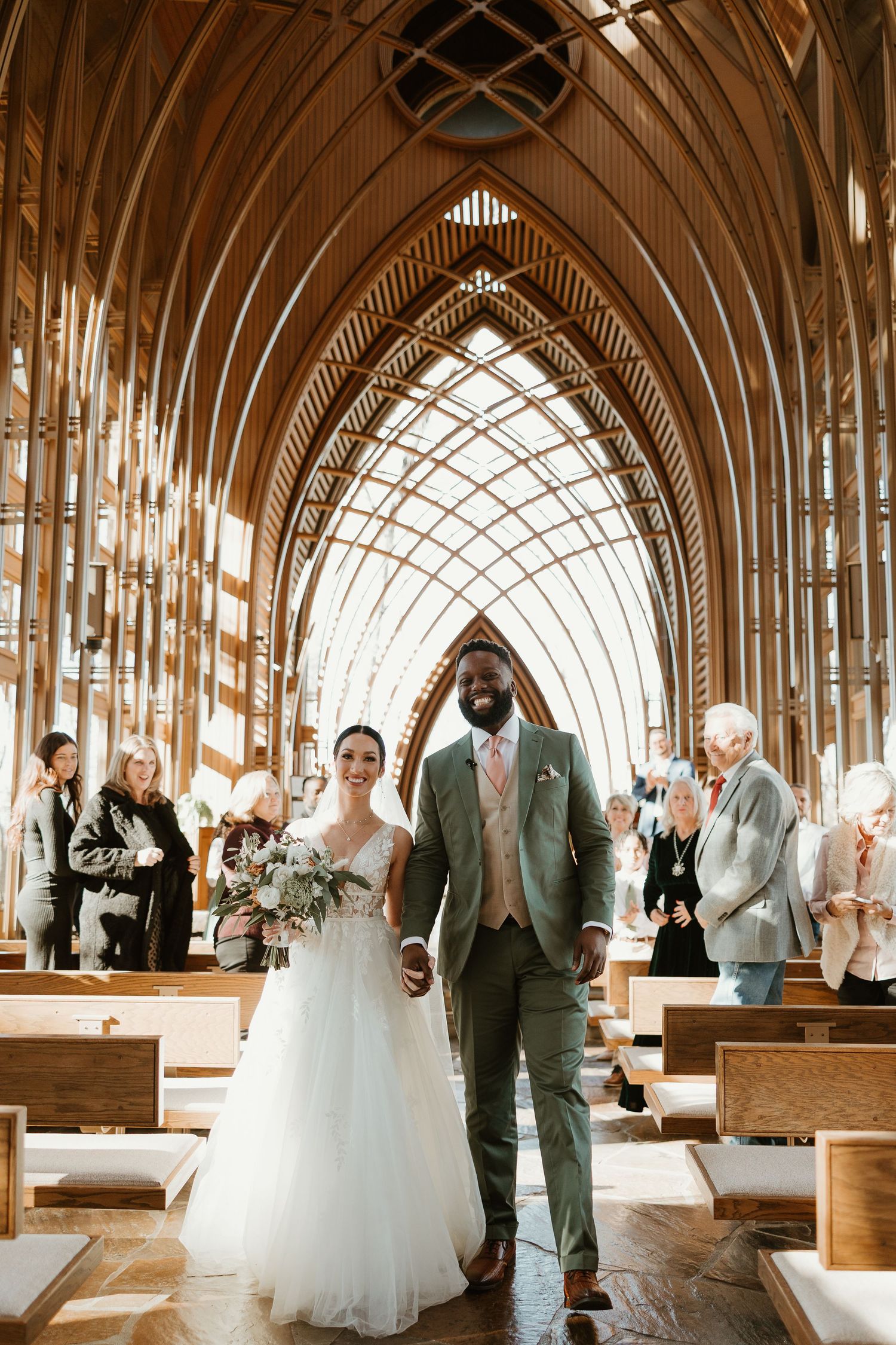 A wedding ceremony takes place in a beautiful chapel with dramatic vaulted wooden arches and natural light streaming in.