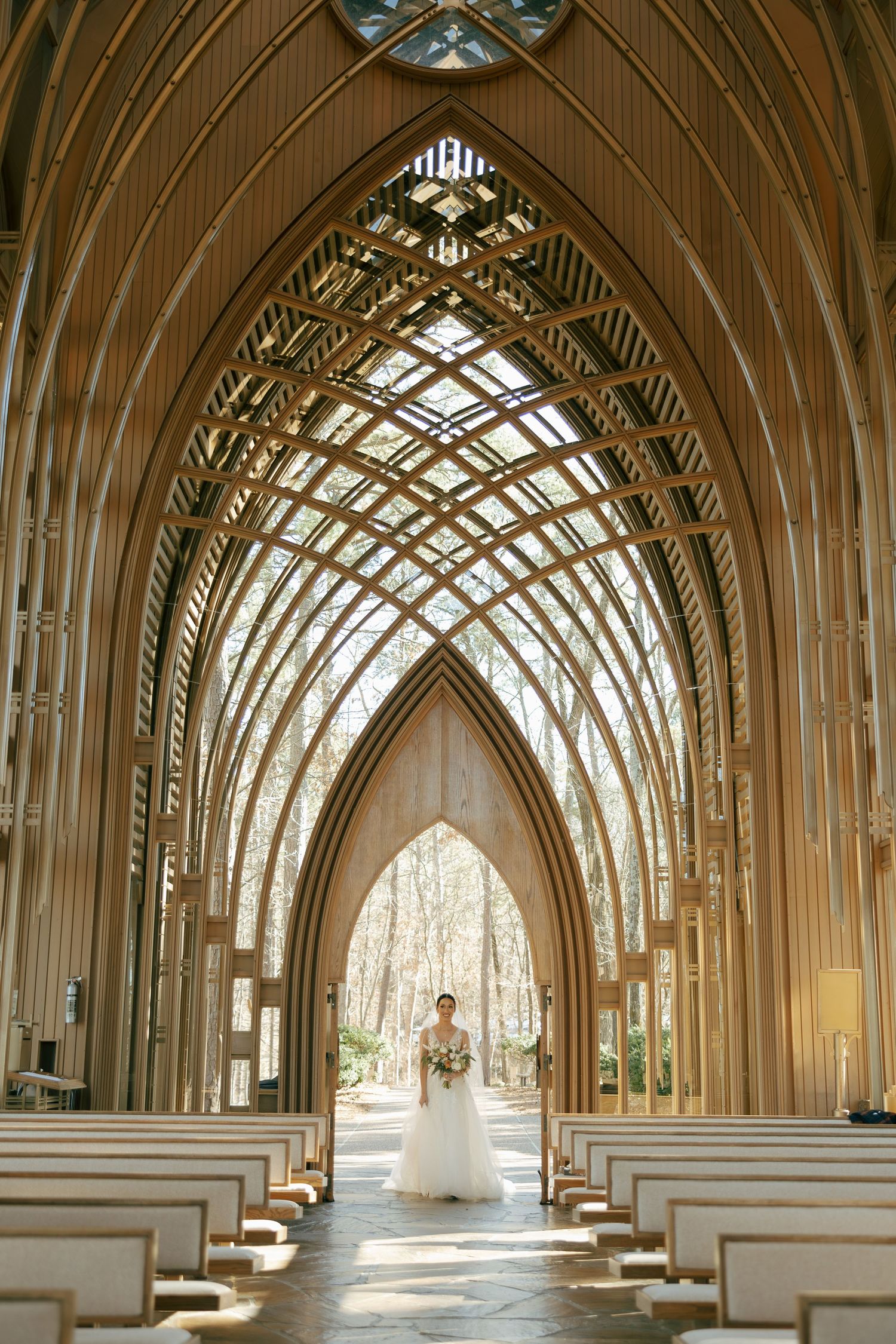 Bride standing at the altar of a stunning Gothic wood and glass chapel with soaring arched ceilings and forest views.