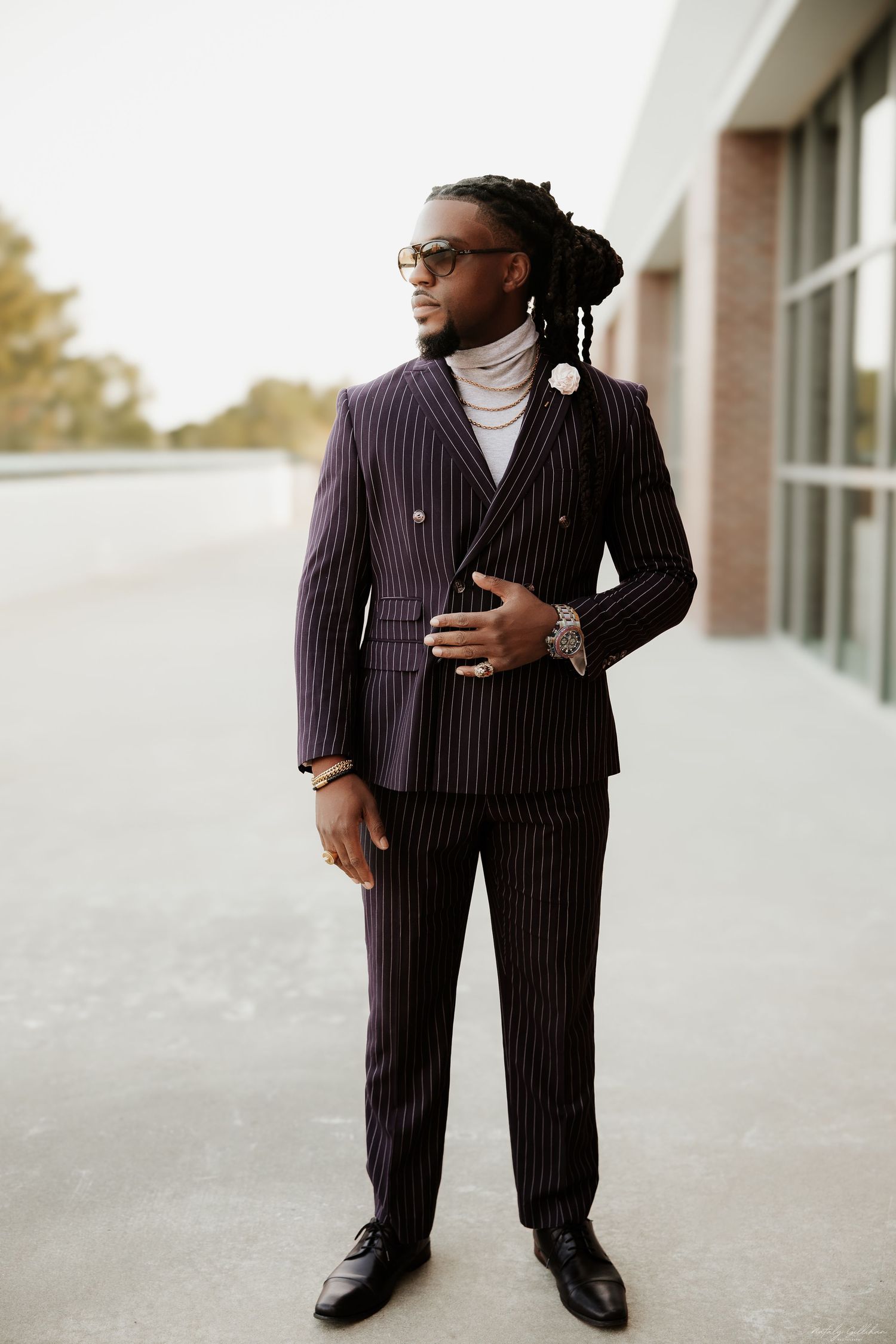 Stylish person wearing a pinstriped double-breasted suit with turtleneck and dress shoes in professional outdoor setting.