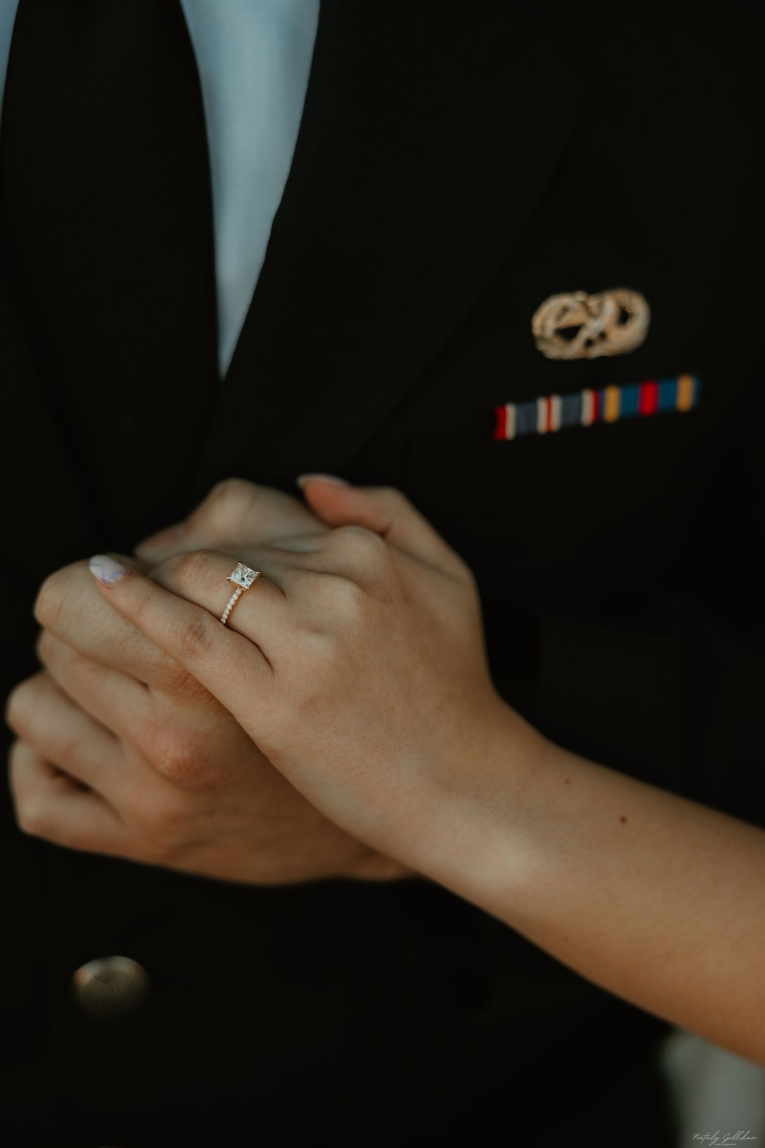 Close-up of joined hands with engagement ring against a military dress uniform.