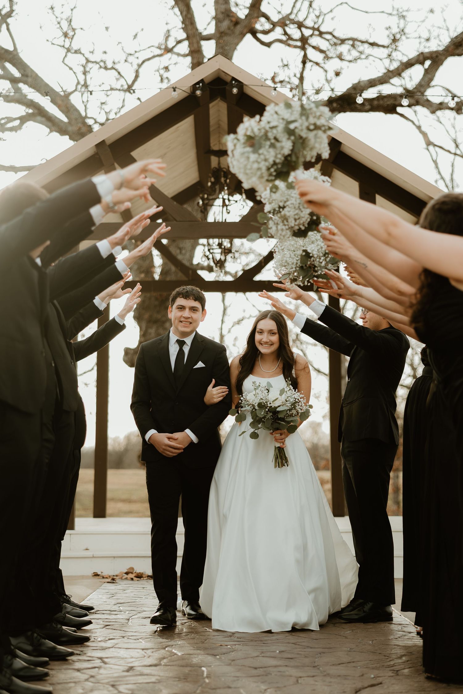 Wedding party members raise champagne glasses in celebration during outdoor ceremony at sunset.
