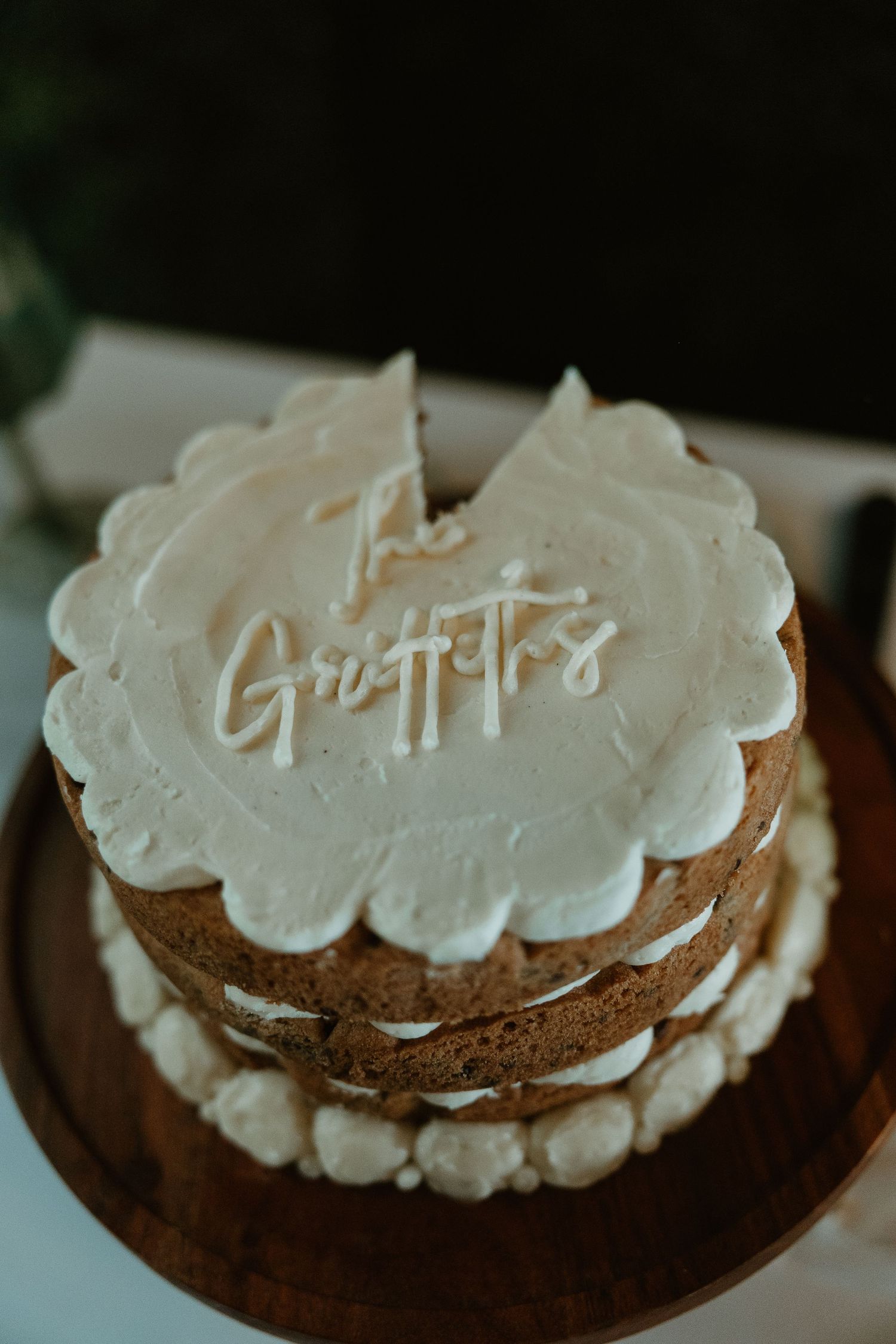 A rustic homemade cake with white frosting and the word 'Gratitude' written on top sits on a dark background.