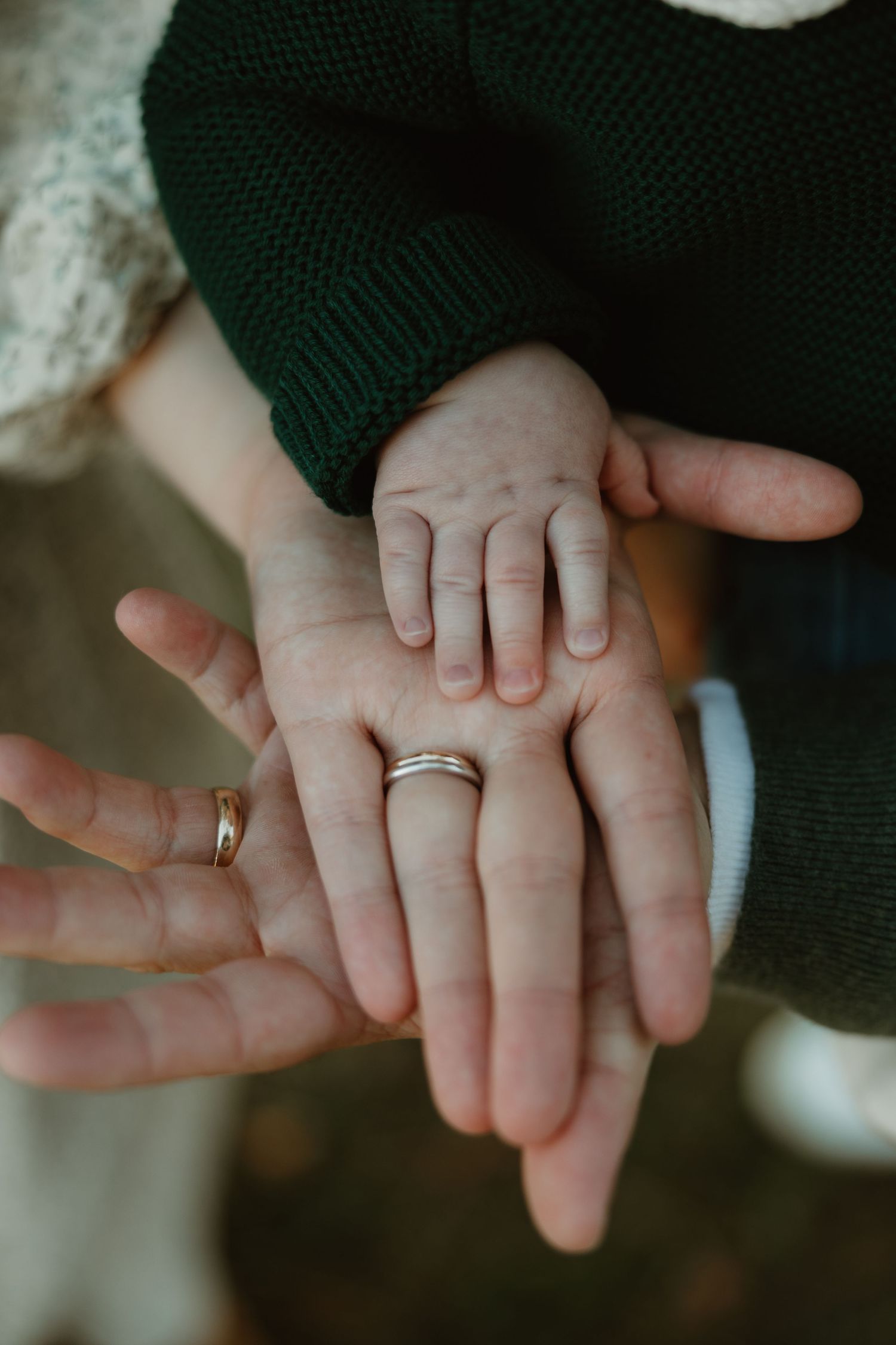 A tiny baby's hand rests gently on an adult's palm wearing a wedding ring, creating a tender family moment.