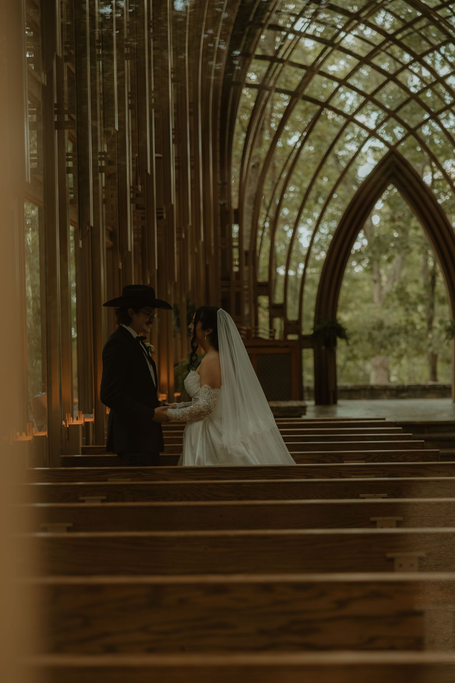 A bride and groom stand at the altar of a stunning glass chapel surrounded by lush greenery on their wedding day.