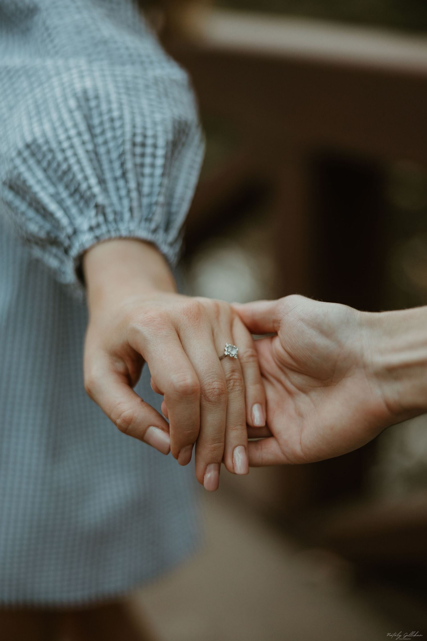 Close-up shot of two hands holding each other tenderly with a diamond engagement ring visible.