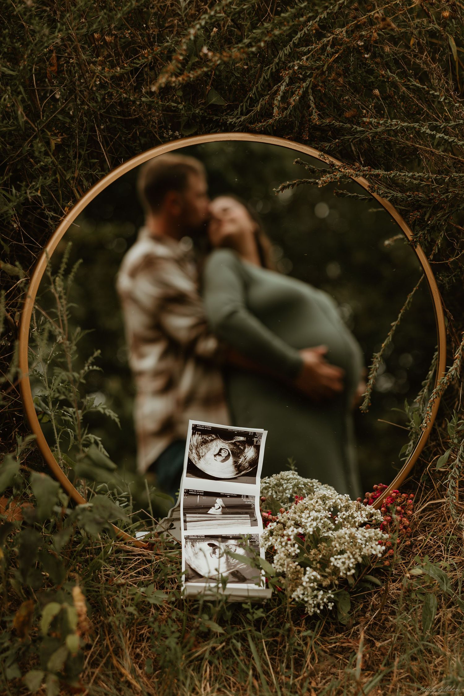 A romantic outdoor pregnancy announcement features ultrasound photos displayed with flowers against a circular golden arch.