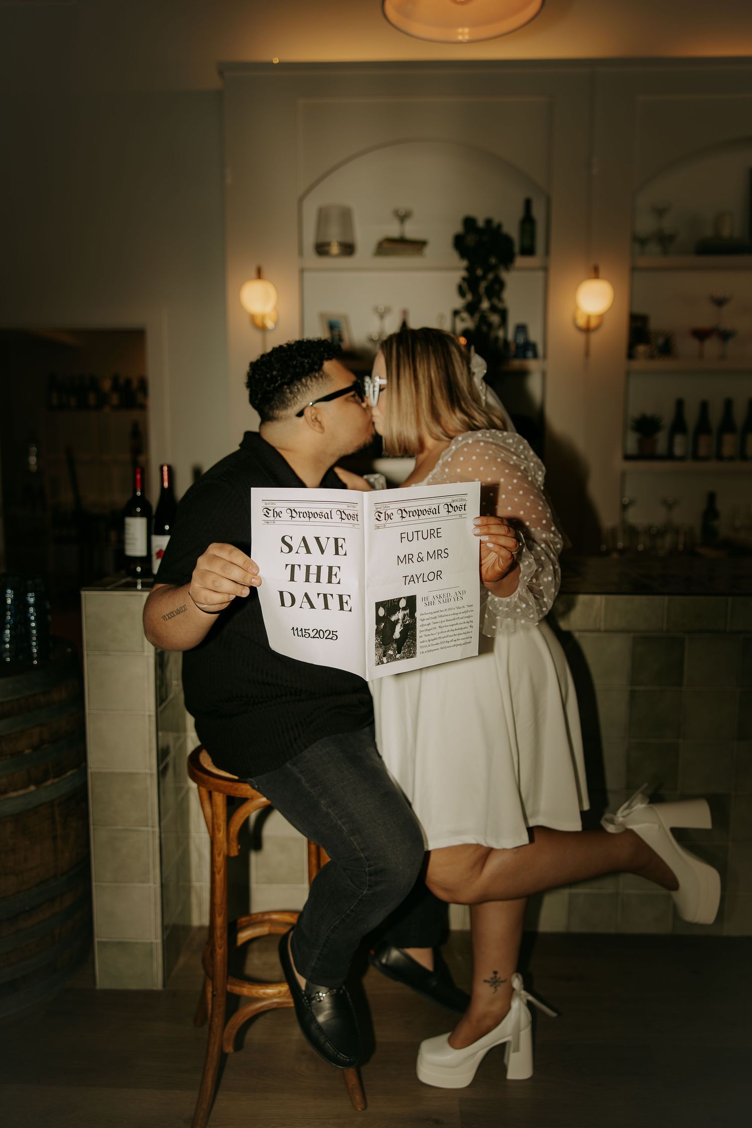 Couple holding newspaper together in dimly lit room creating engagement announcement photo sequence.