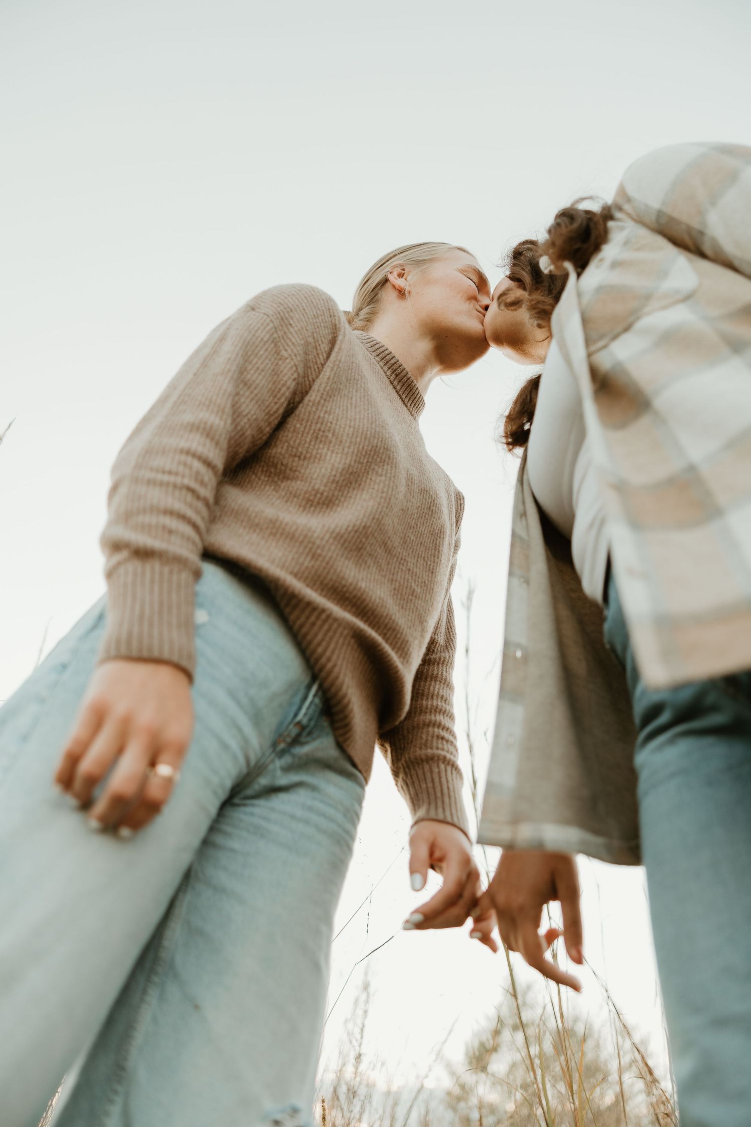 A romantic couple in casual sweaters embraces and kisses in a soft, dreamy outdoor setting.
