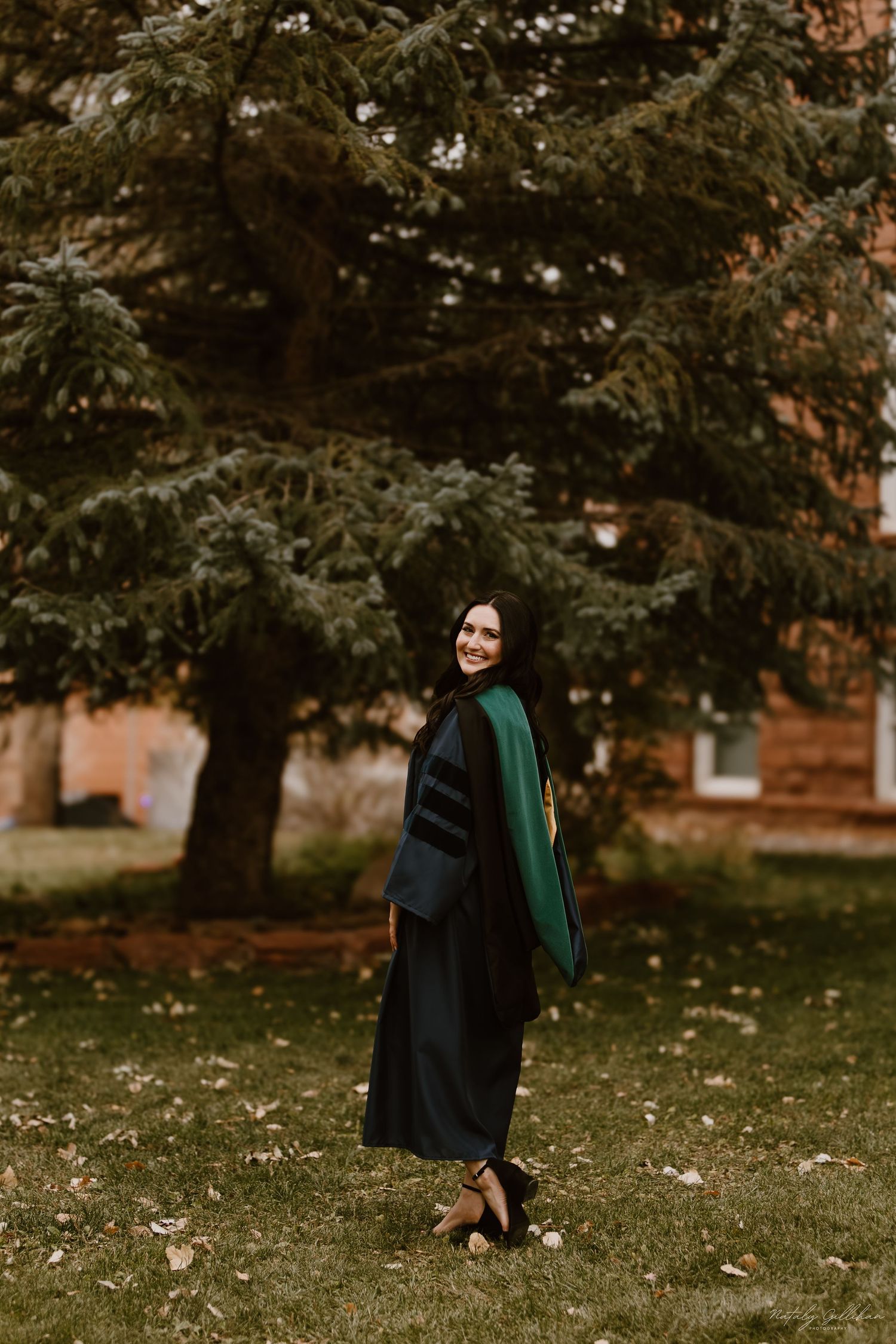 A person in a dark dress and emerald green shawl poses gracefully on an autumn lawn with trees in the background.
