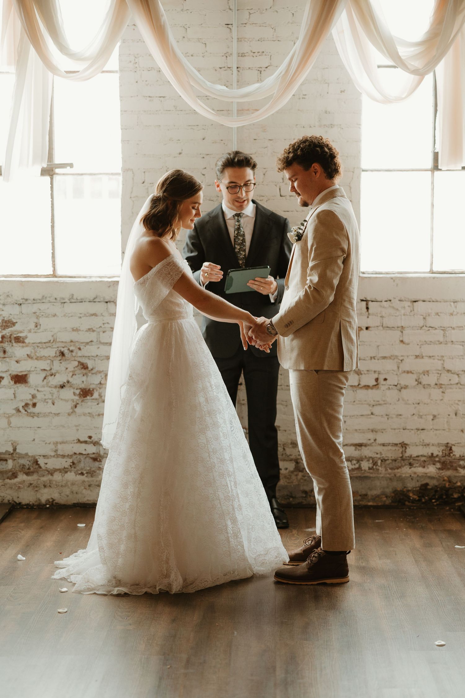 An intimate wedding ceremony in a rustic white brick venue with hardwood floors shows couples exchanging vows.