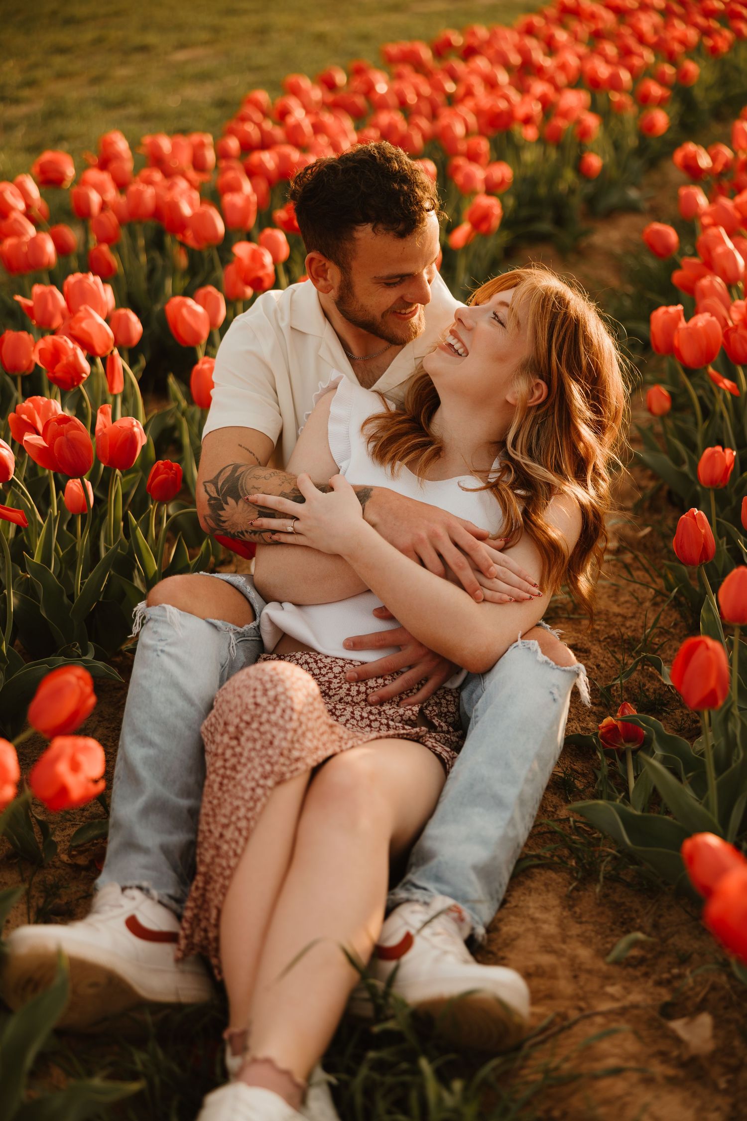 A romantic moment shared between a couple sitting among vibrant red tulips in a garden during golden hour.
