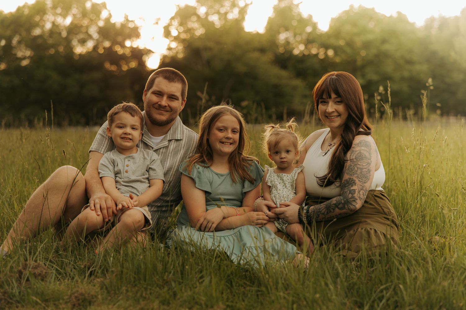 Family sitting together in a golden sunlit meadow at sunset dressed in neutral earth tones.