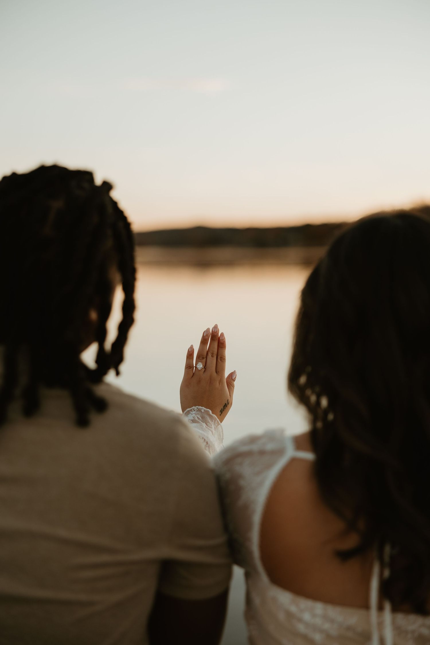 A silhouetted figure raises their hand against a serene lakeside sunset backdrop.