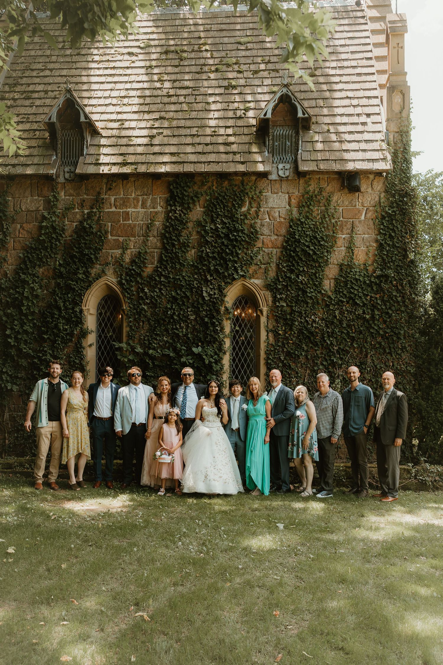 A wedding party poses in front of a stone church building covered in climbing ivy vines.