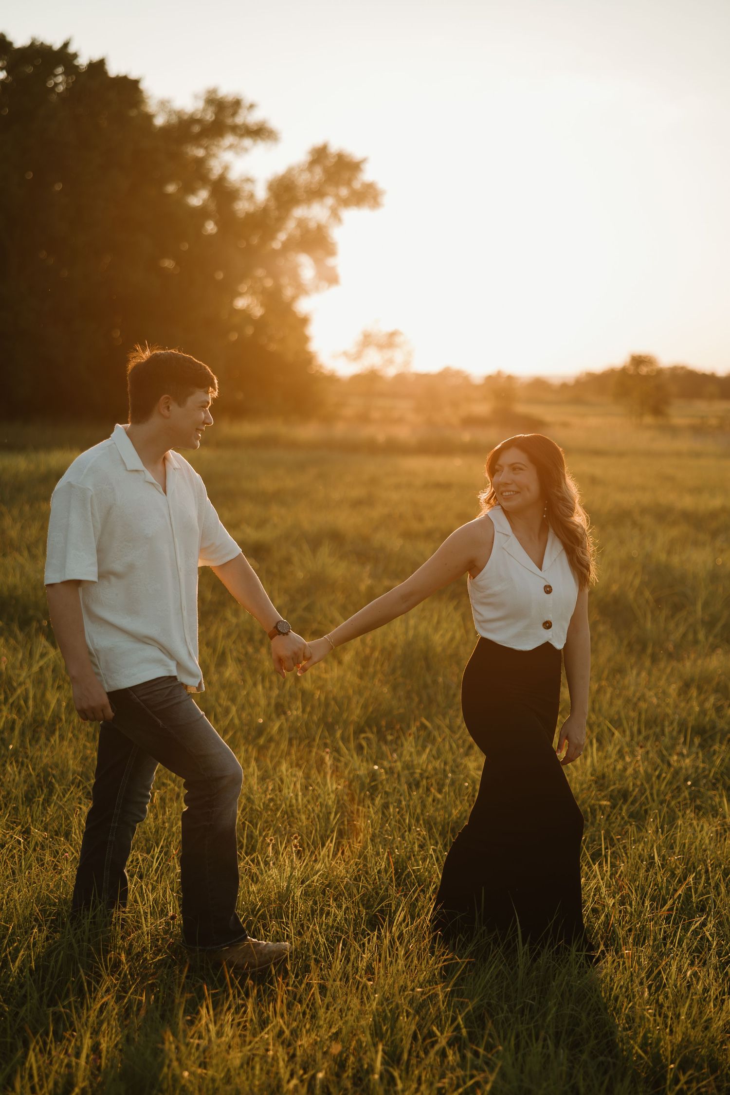 Couple dancing together in golden sunlit meadow at sunset creating romantic silhouettes against warm evening light.
