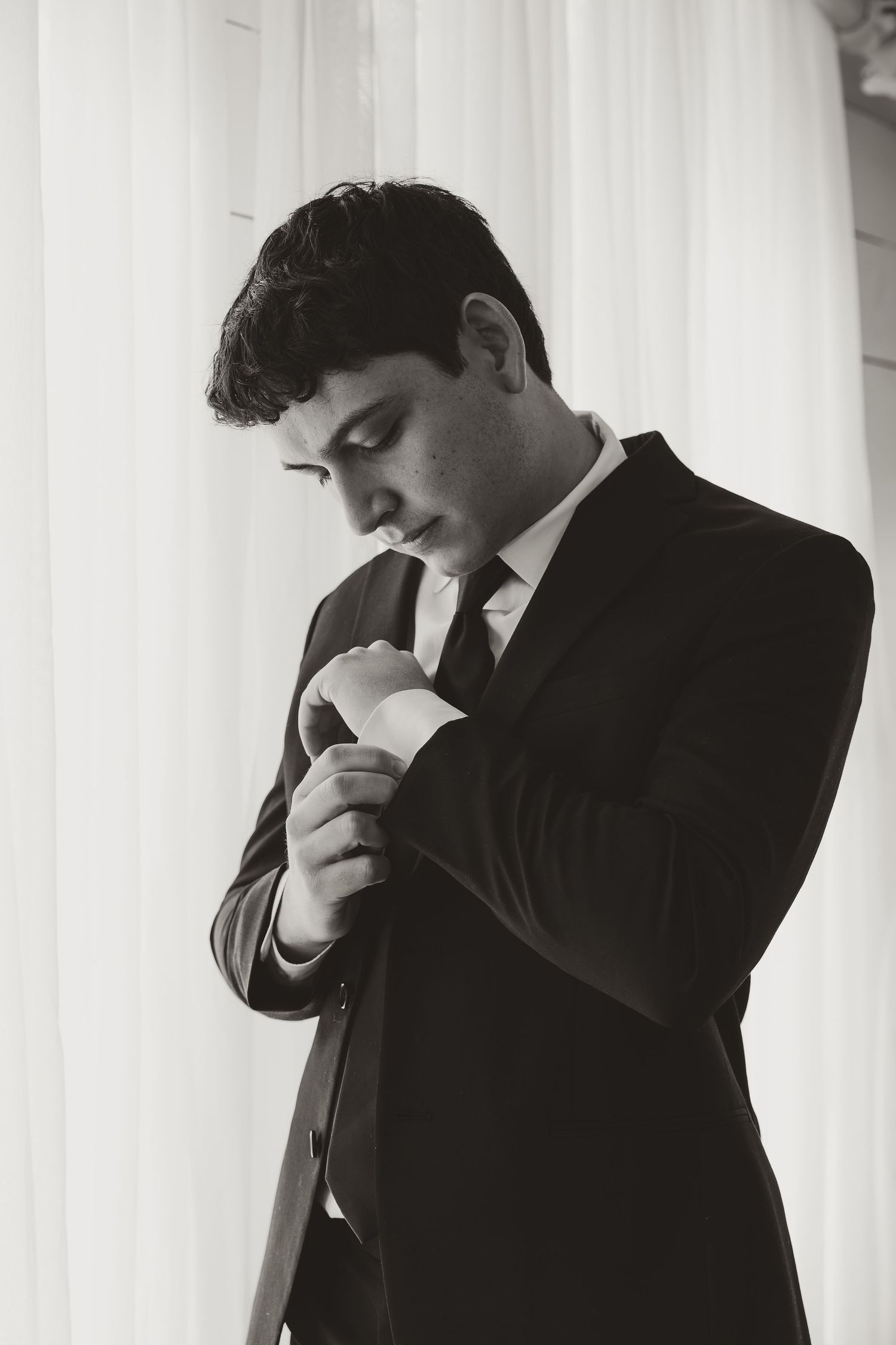 Black and white portrait of a person in formal attire looking down thoughtfully against a light background.
