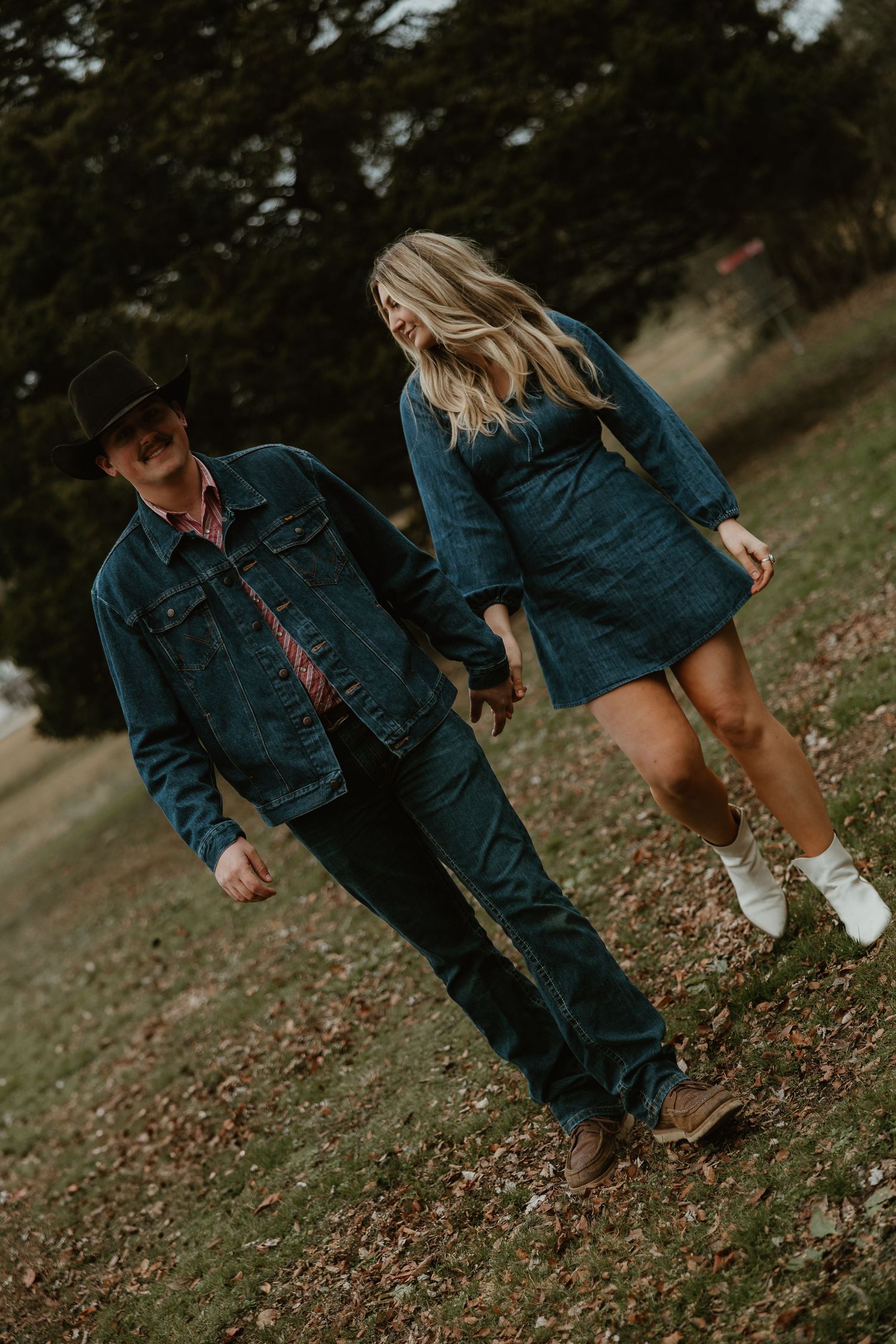 People wearing denim outfits walk through fallen autumn leaves in a park setting during an outdoor photoshoot.