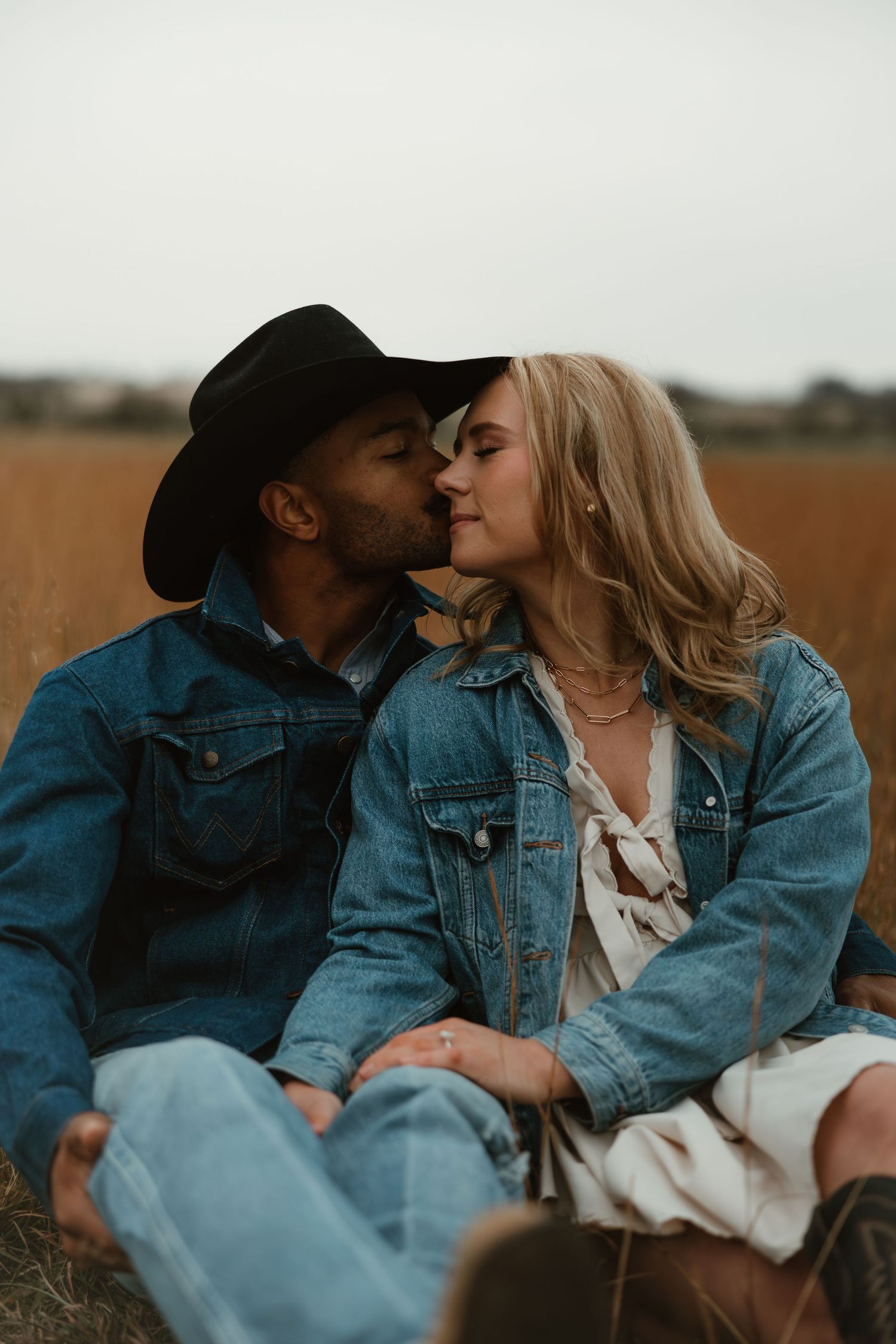 A romantic couple in denim jackets share tender moments together in a rustic outdoor field setting.