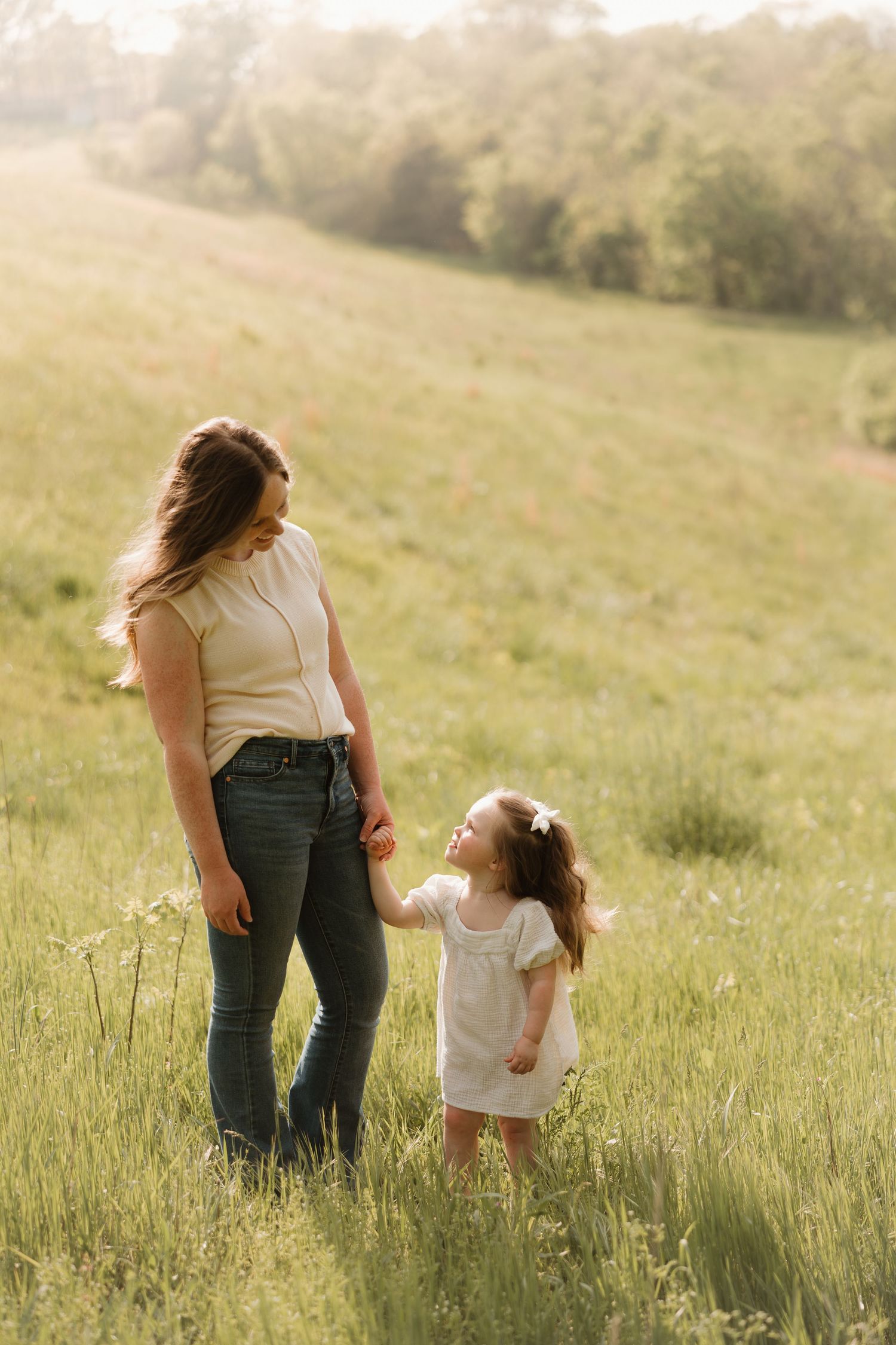 A mother and daughter share a tender moment together in a sunlit meadow during golden hour.