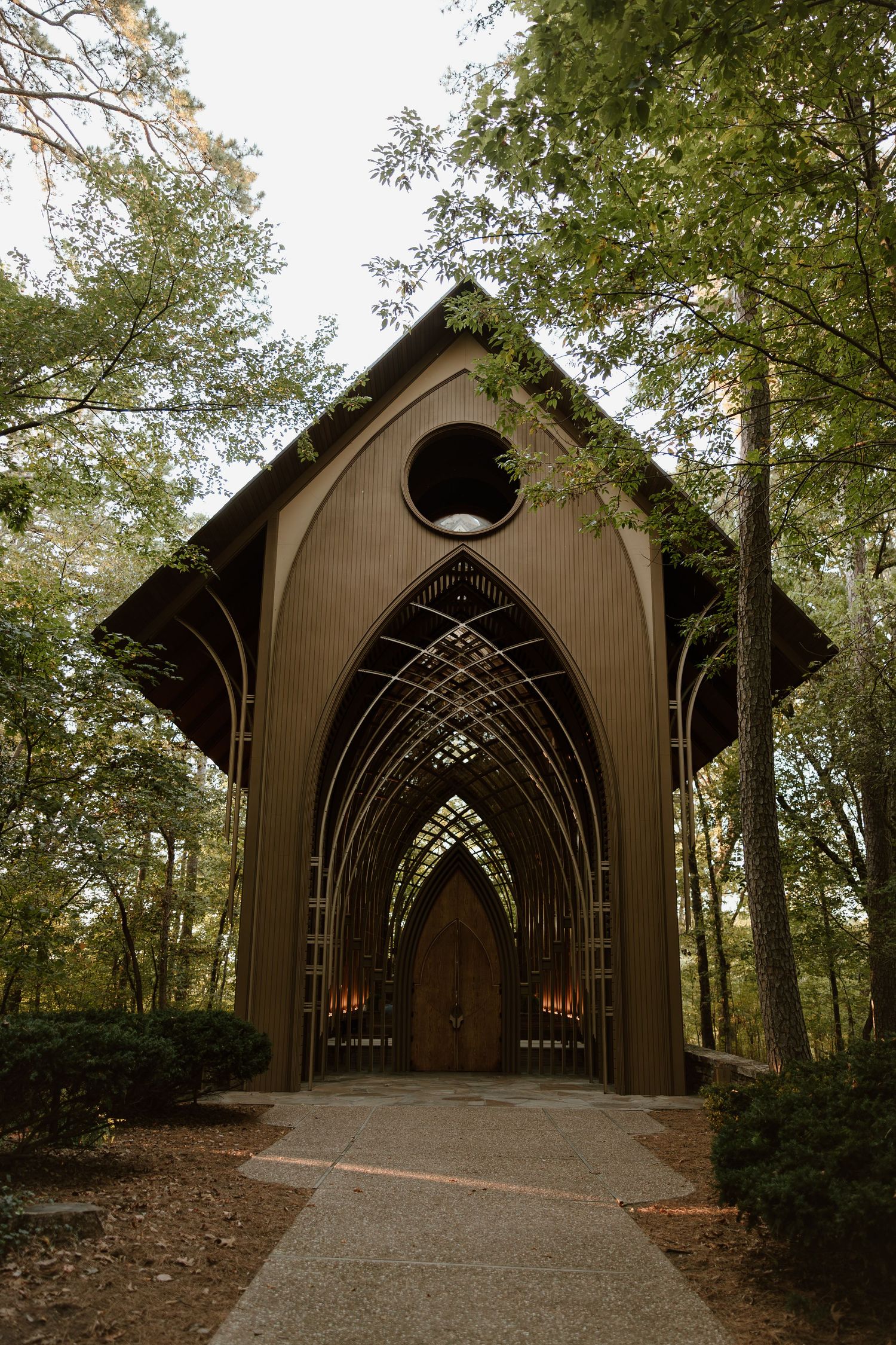 A series of four photos showing a wooden Gothic-style chapel entrance with arched doorways nestled in a wooded setting.