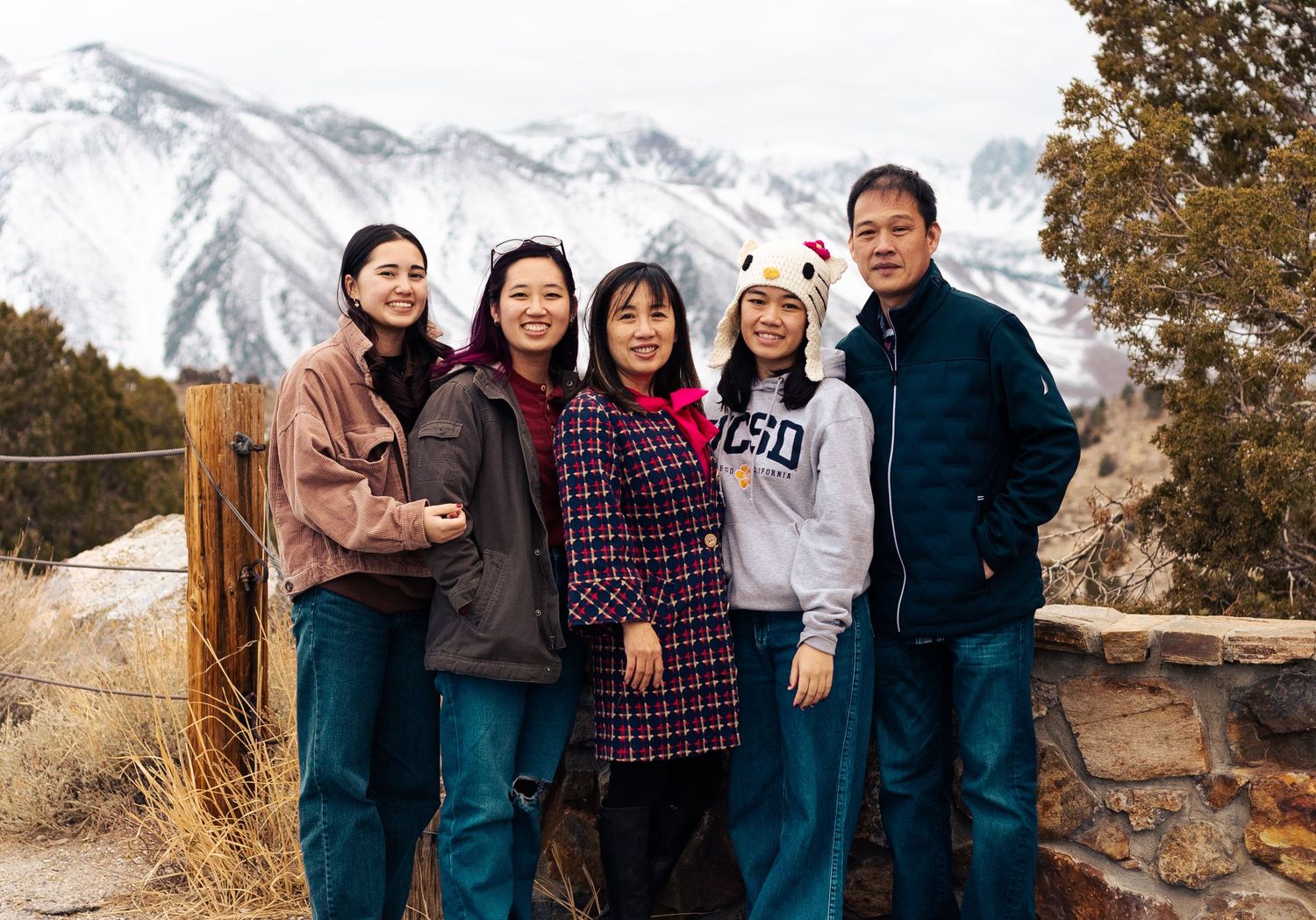 A group of people stand together outdoors against a backdrop of snow-capped mountains and autumn foliage.