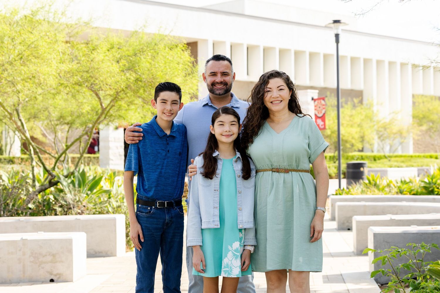 Family of four smiling outdoors near modern building, parents with two children dressed in smart casual attire.
