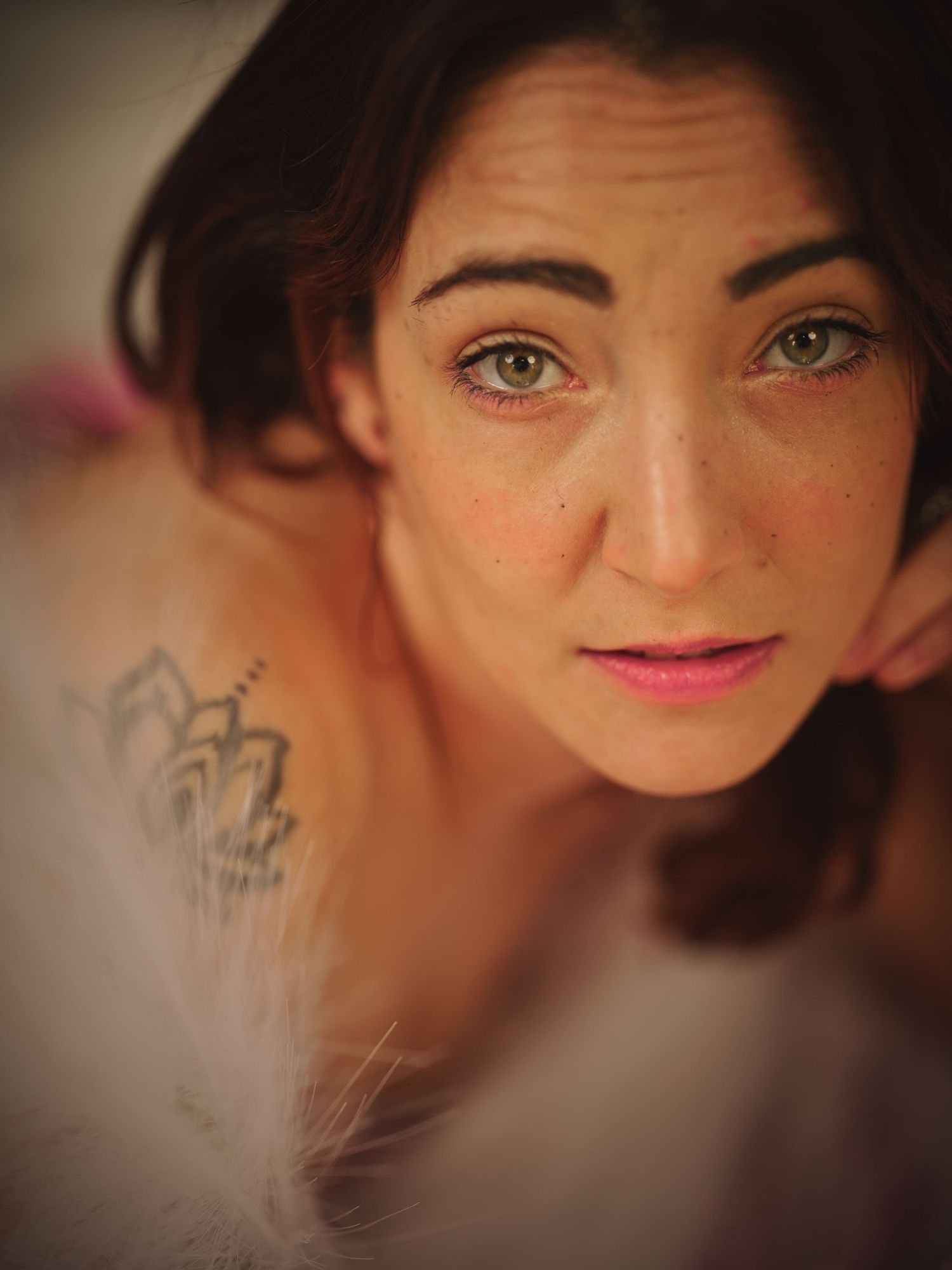 Portrait with dark hair and expressive green eyes with a partially visible tattoo on the shoulder.