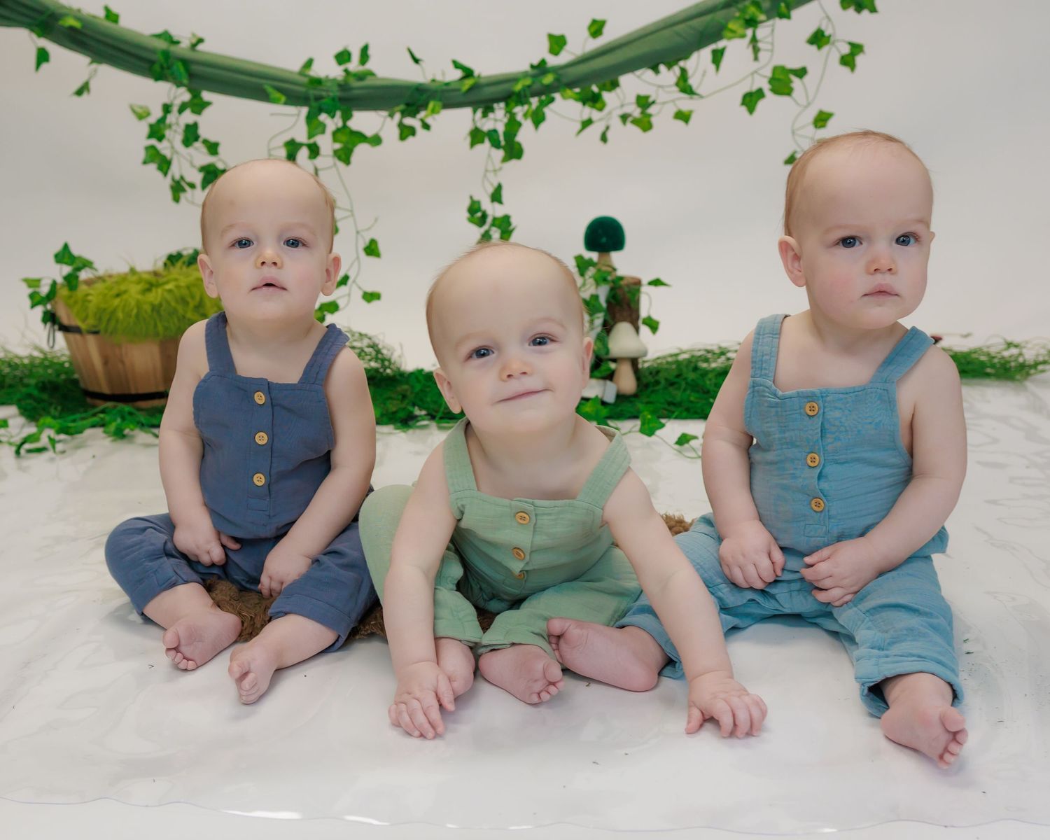 A progression of images showing babies in blue overalls sitting and crawling against a white background with green vine decorations.