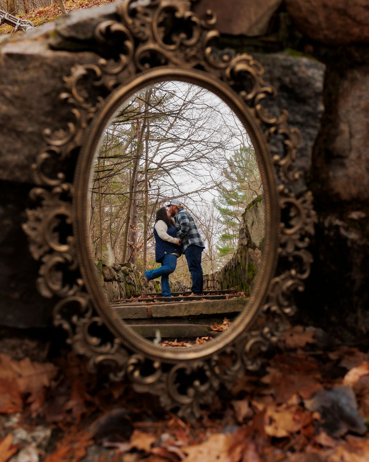 Romantic couple reflected in ornate vintage mirror frame surrounded by autumn leaves.