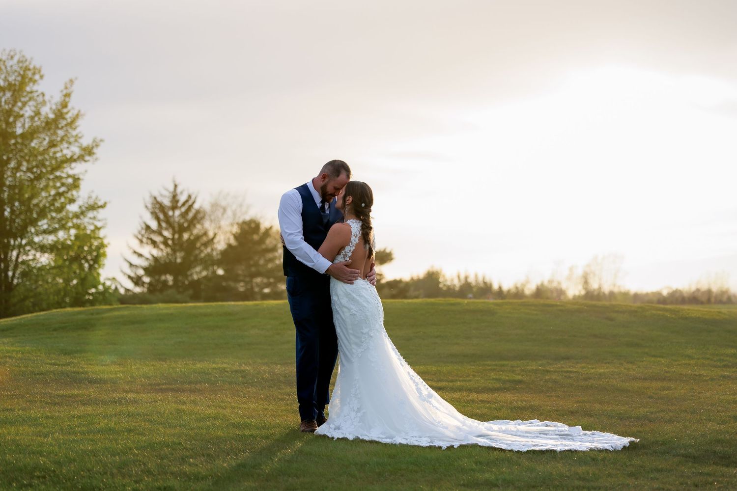 Bride and groom share a romantic kiss at sunset on a lush green golf course, bride in elegant white gown.