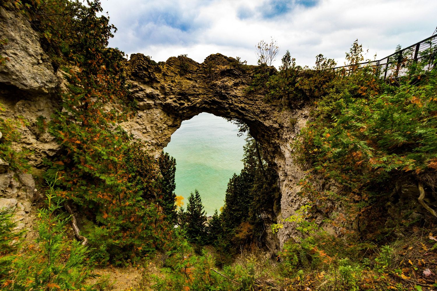 Scenic view of Natural Bridge spanning over turquoise water at Mackinac Island with rocky cliffs and green foliage.