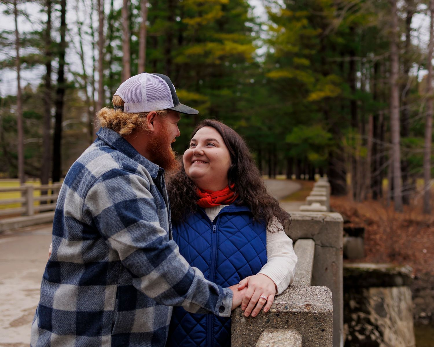 A couple shares a joyful moment together while leaning on a stone wall in a wooded nature setting.