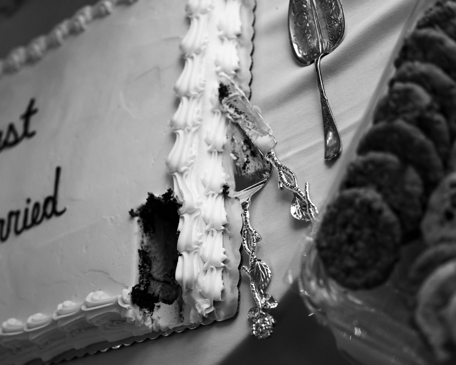 Black and white close-up image of a wedding cake with ornate white frosting details and decorative edging.