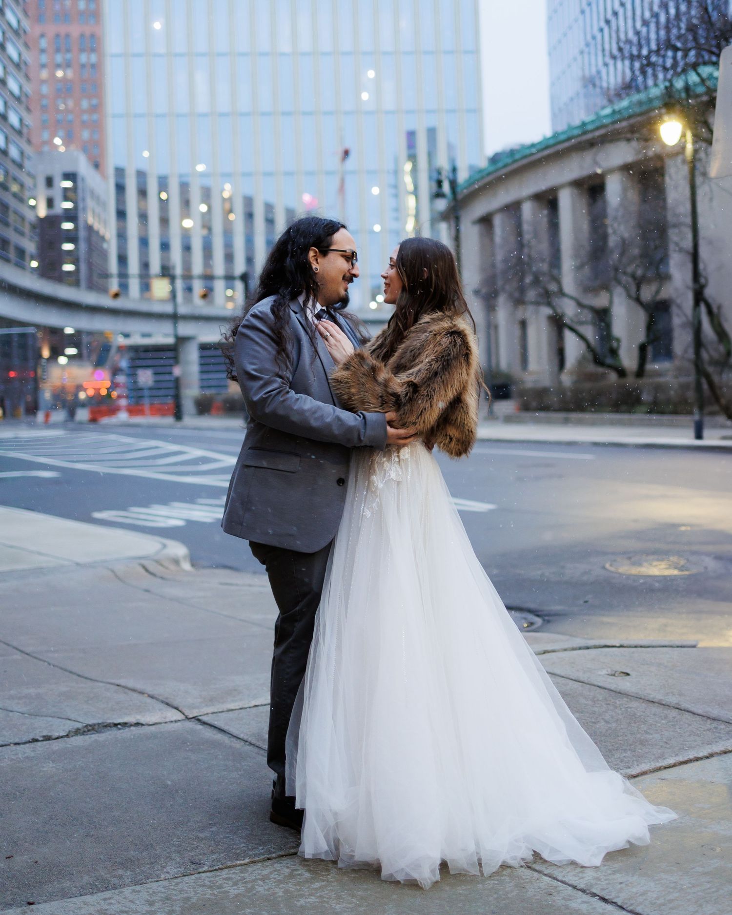 A couple in wedding attire dances together on a city street during golden hour.