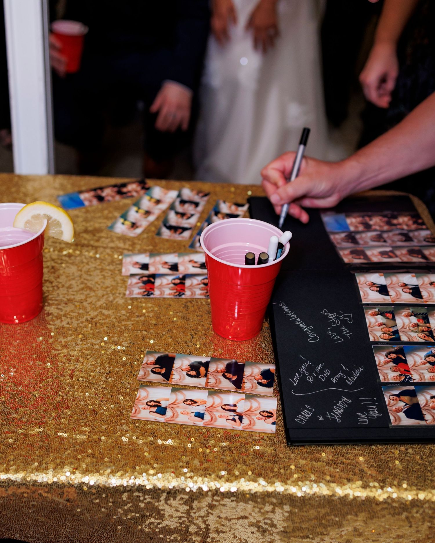 A gold sequined tablecloth with photo strips and red cups laid out for a party setting.