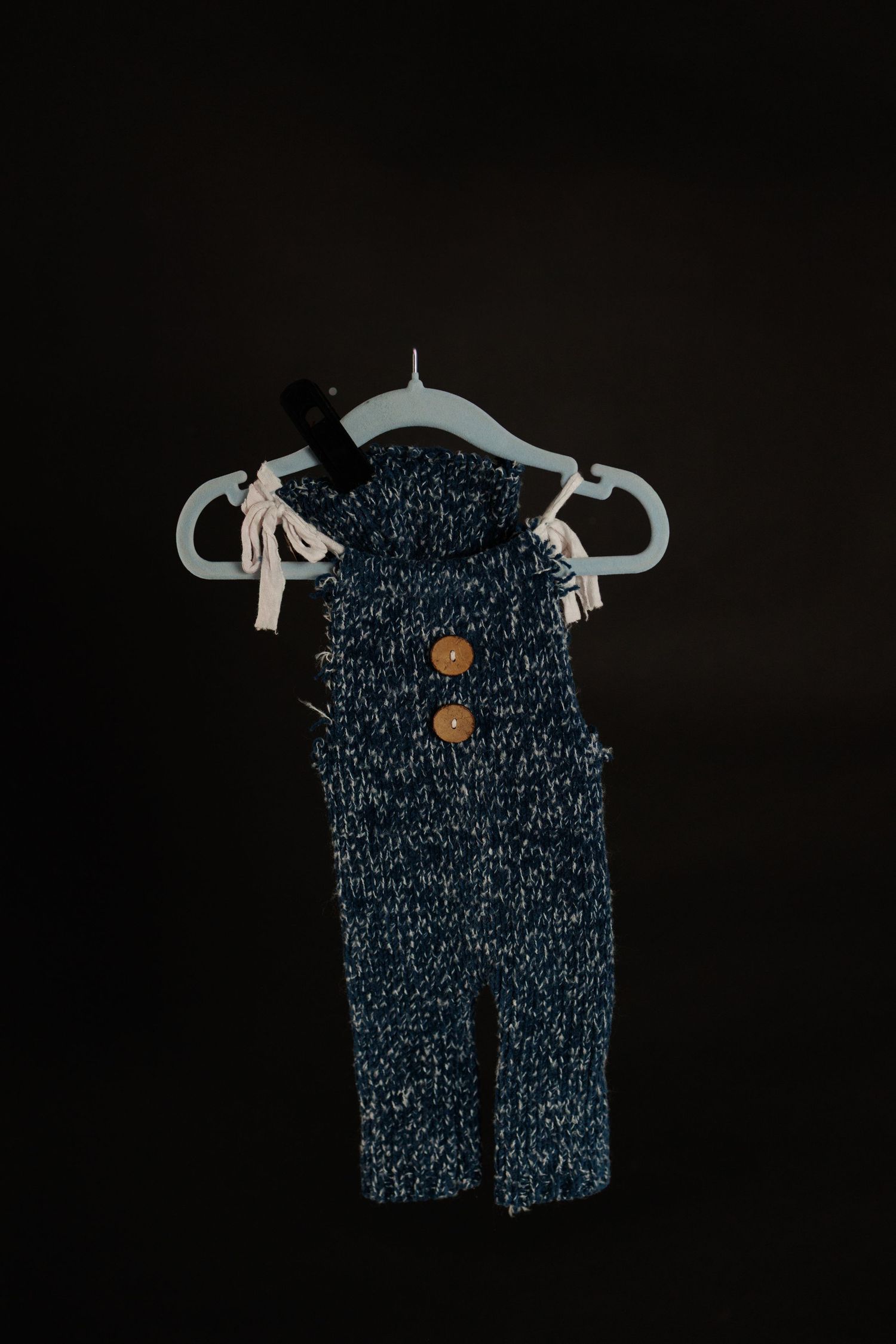 A dark blue baby romper with white speckled pattern hangs on a hanger against a black background.