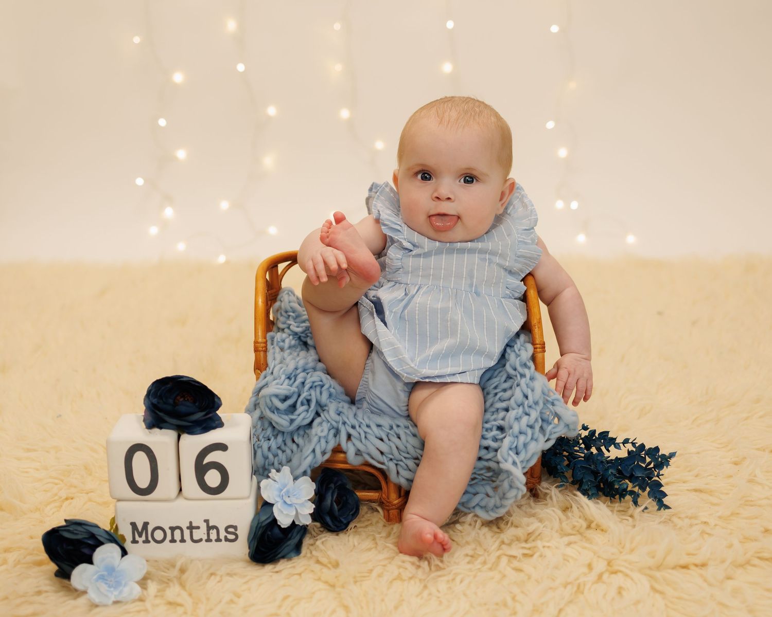 A series of infant milestone photos on a cream background showing growth at 6 months posing with blue accessories.
