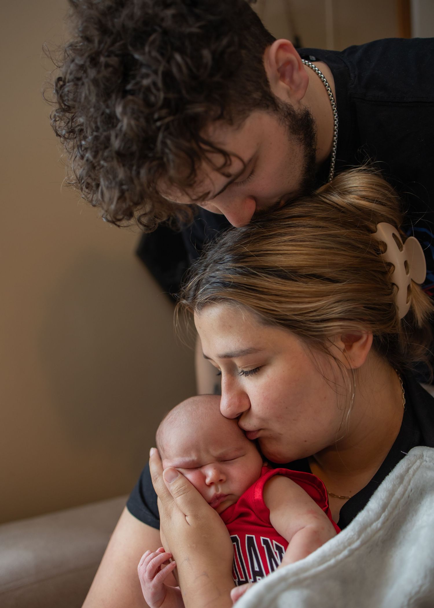 A tender family moment as parents share a quiet moment with their sleeping newborn baby wearing red.