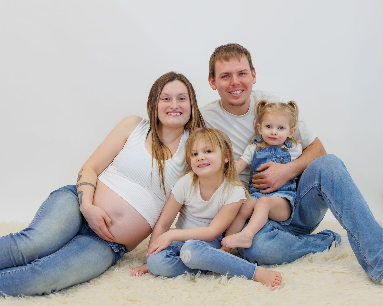 A family in matching denim sits together on white carpet for a casual portrait session.