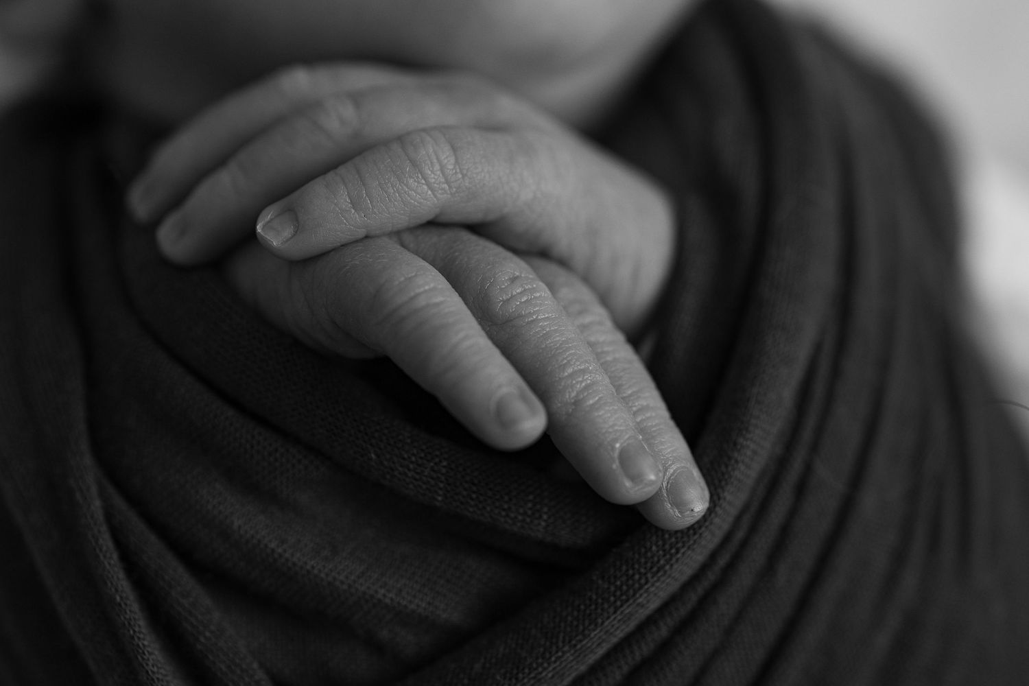 Black and white close-up photo showing hands resting on dark fabric with dramatic shadows and contrast.