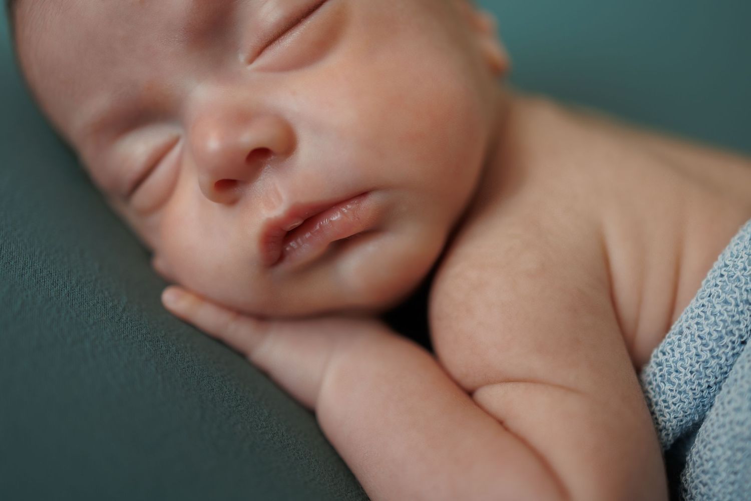 Peaceful sleeping newborn baby rests on teal cushion with soft natural lighting.