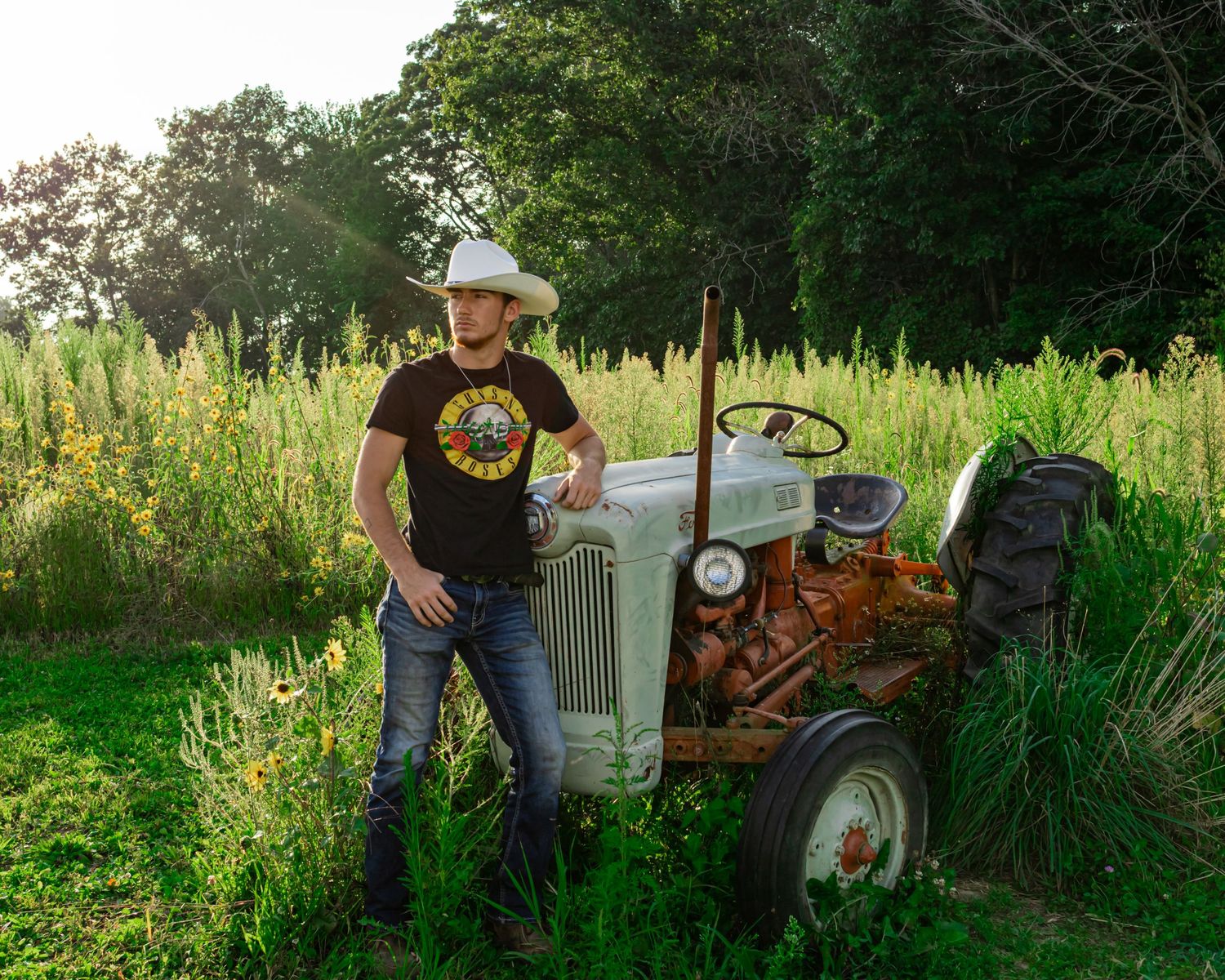 Old Ford tractor in a lush green field with wildflowers at sunset.