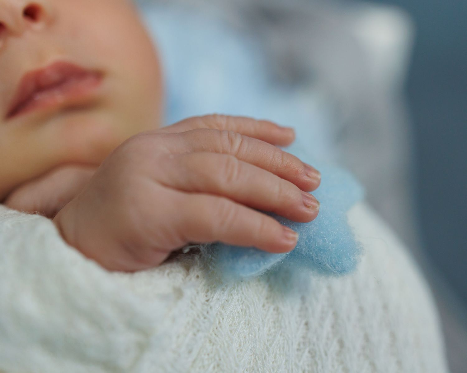 Close-up of a tiny hand resting on soft blue and white fabric.