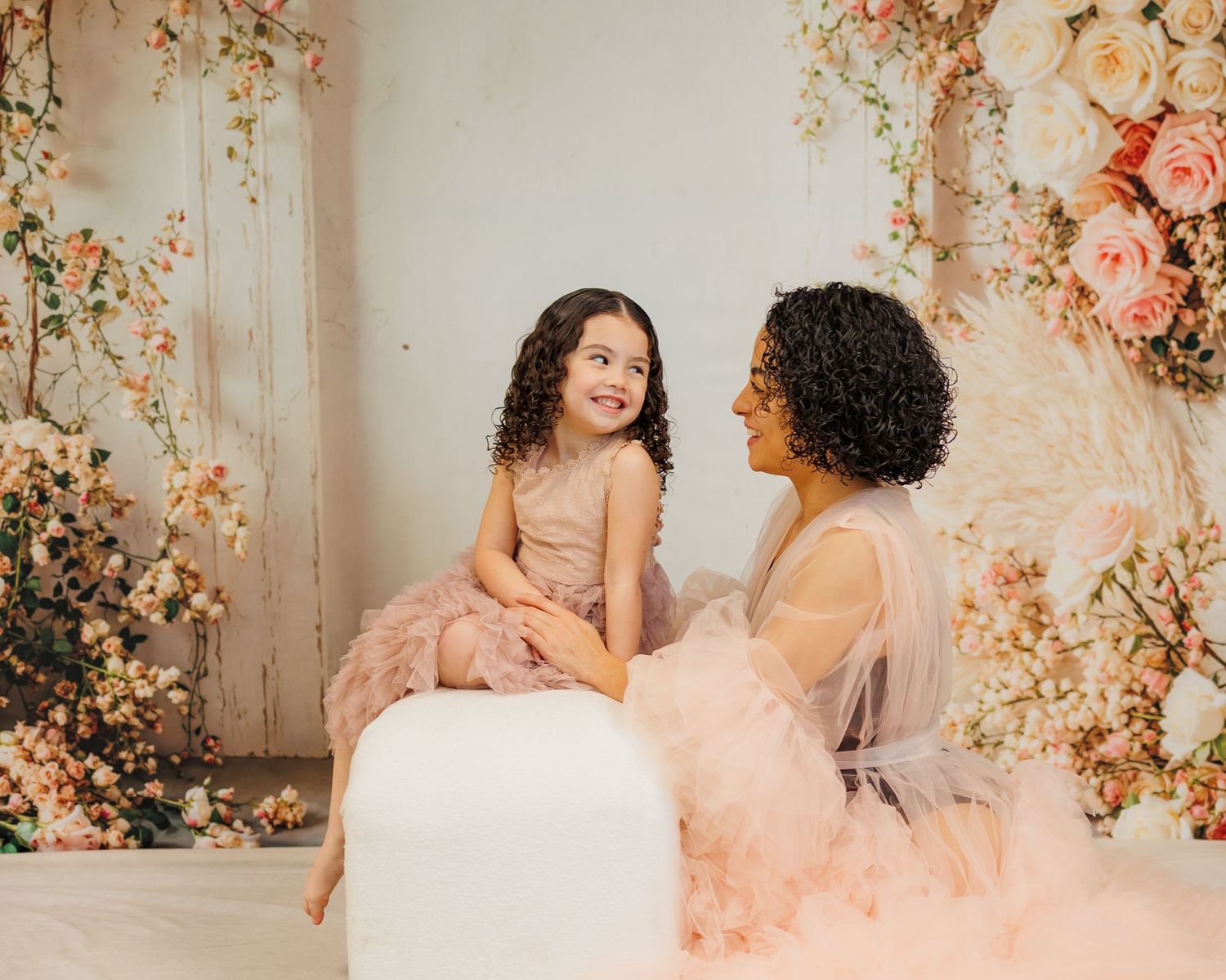 Two people share a tender moment surrounded by romantic floral decor and soft peach-colored drapery.