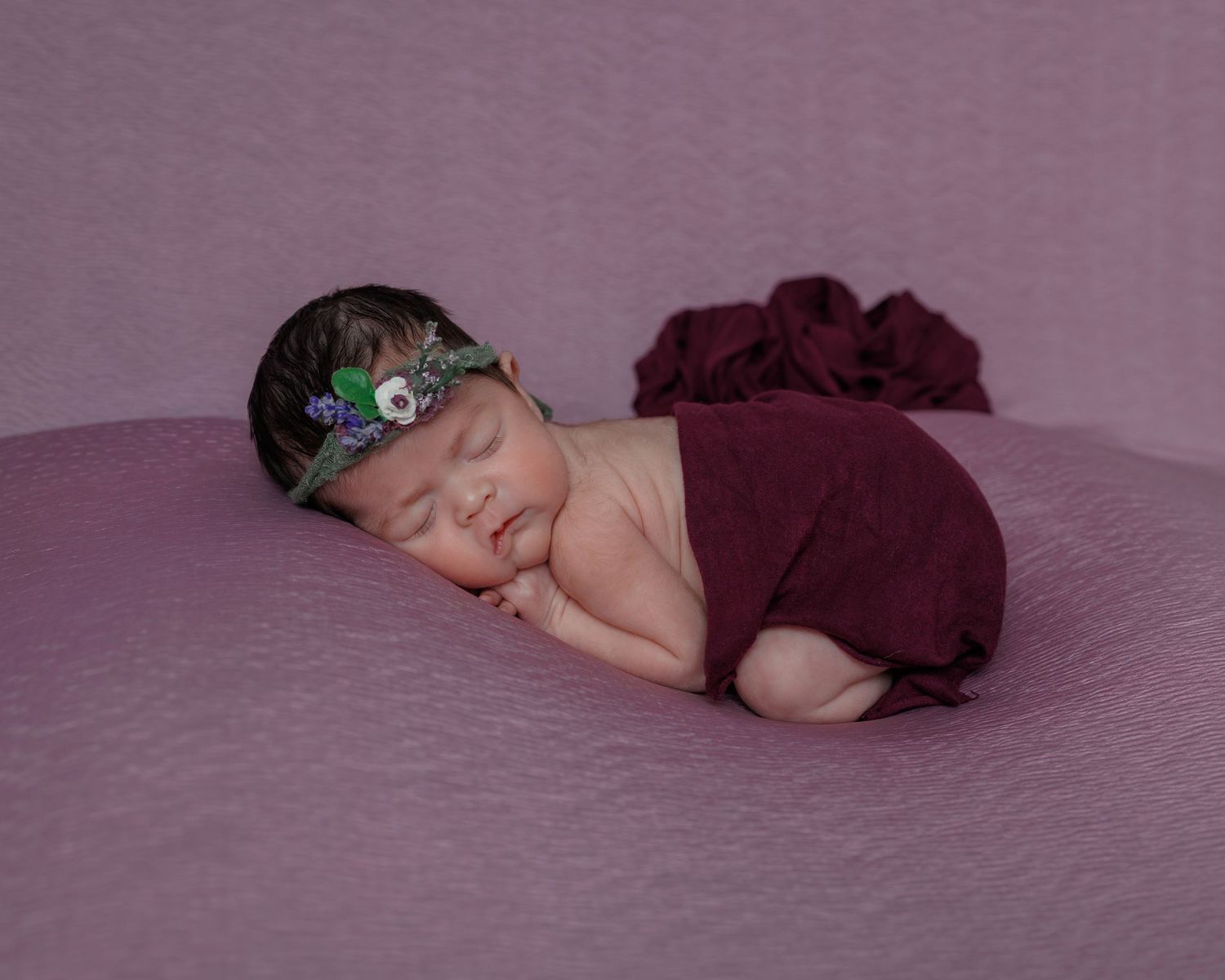 Seven sequential photos show a sleeping baby in a burgundy wrap posed against a lavender backdrop during a newborn photography session.