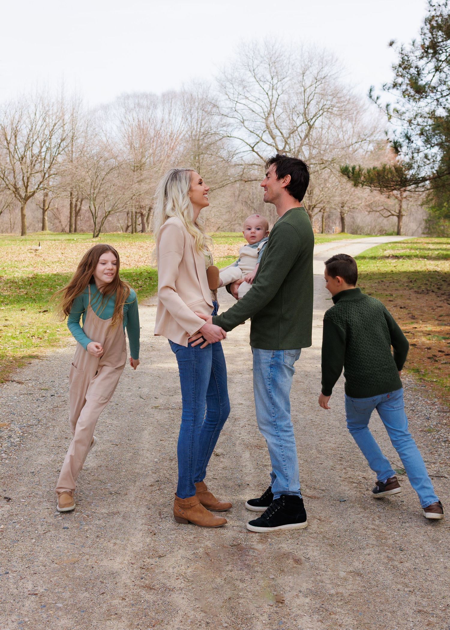 A family enjoying a casual stroll together on a dirt path surrounded by bare winter trees on a sunny day.