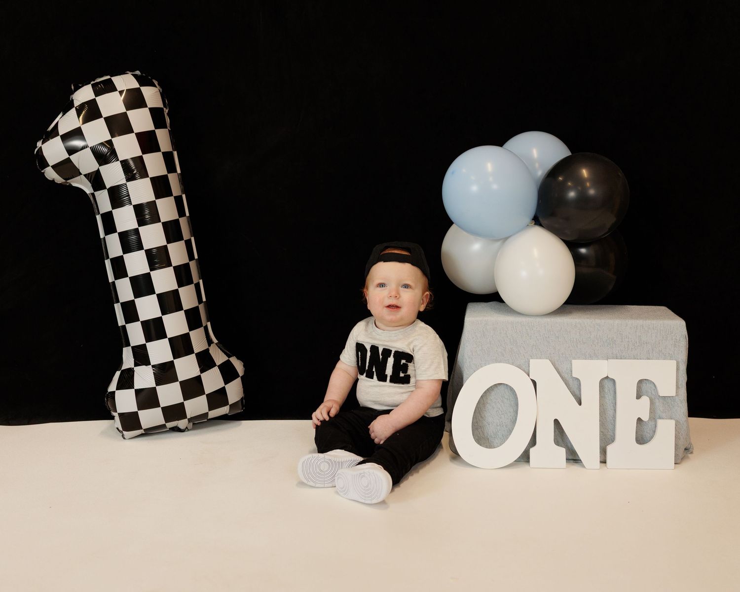 A plain black backdrop and checkered balloon are the perfect backddrop for a boys first birthday photoshoot in my cozy Attica studio.