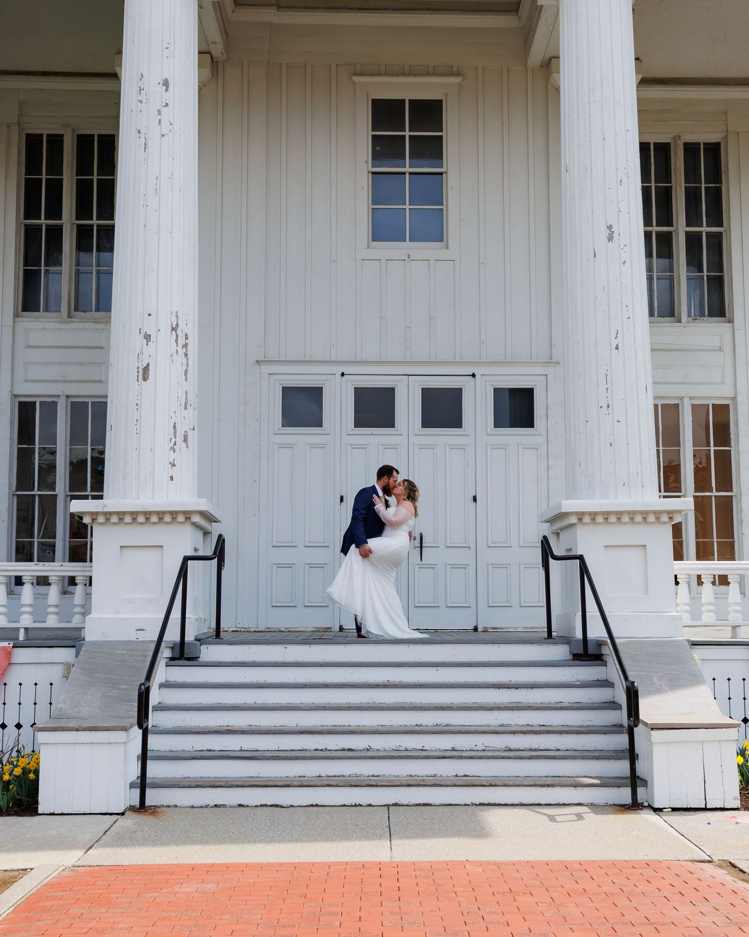 Wedding couple shares a romantic kiss on a white porch with classic columns at an elegant historic mansion.
