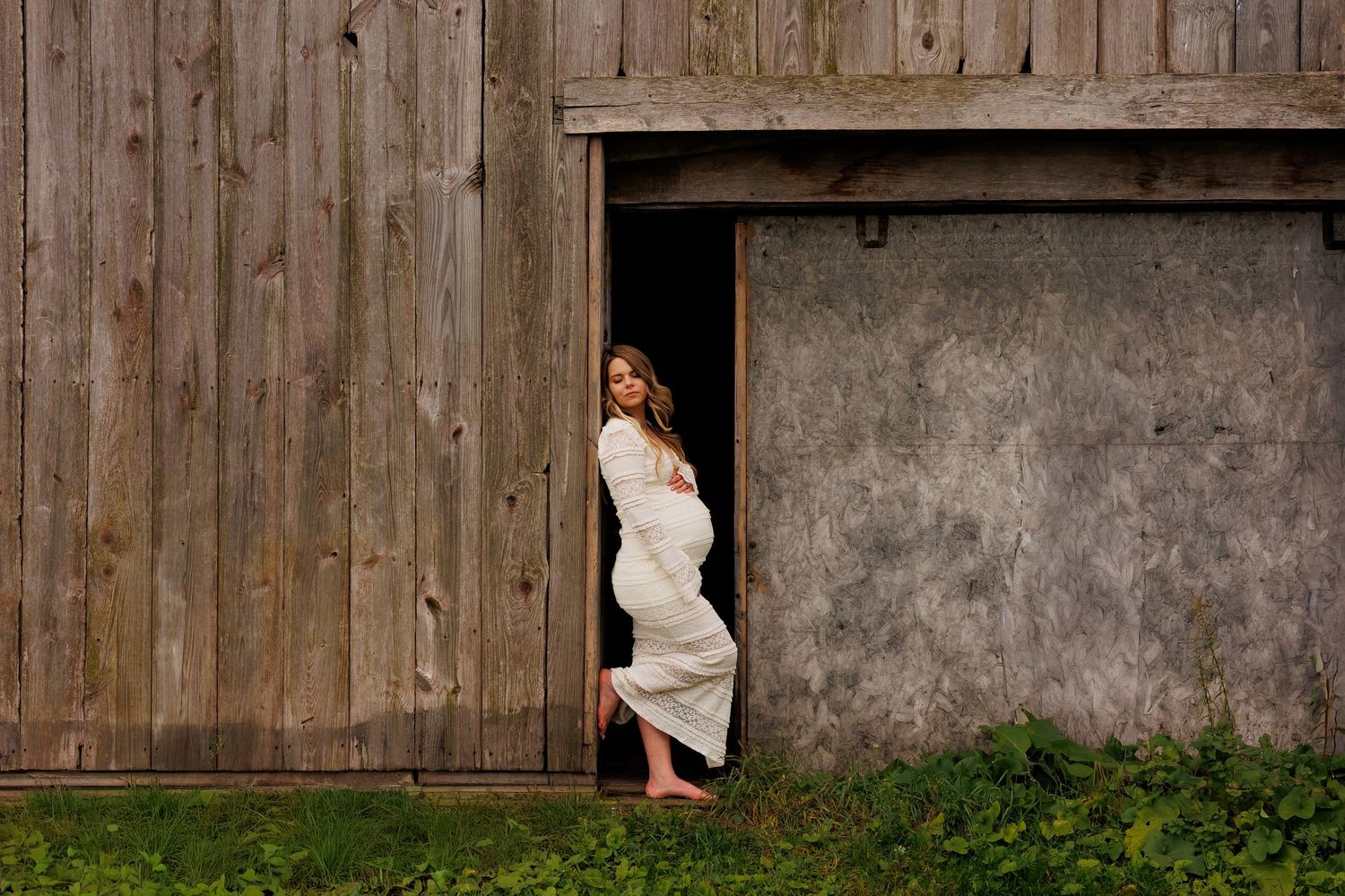 A rustic barn wedding photoshoot features a white dress against weathered wooden walls and natural lighting.