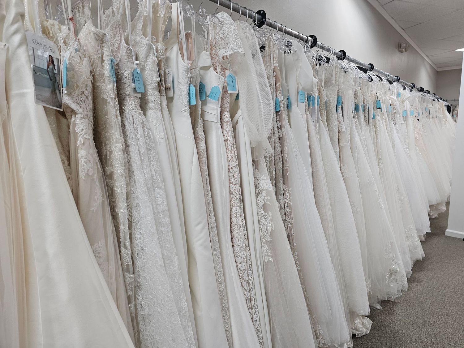Long rack of white wedding dresses displayed in a bridal shop with tulle and lace gowns hanging in rows.